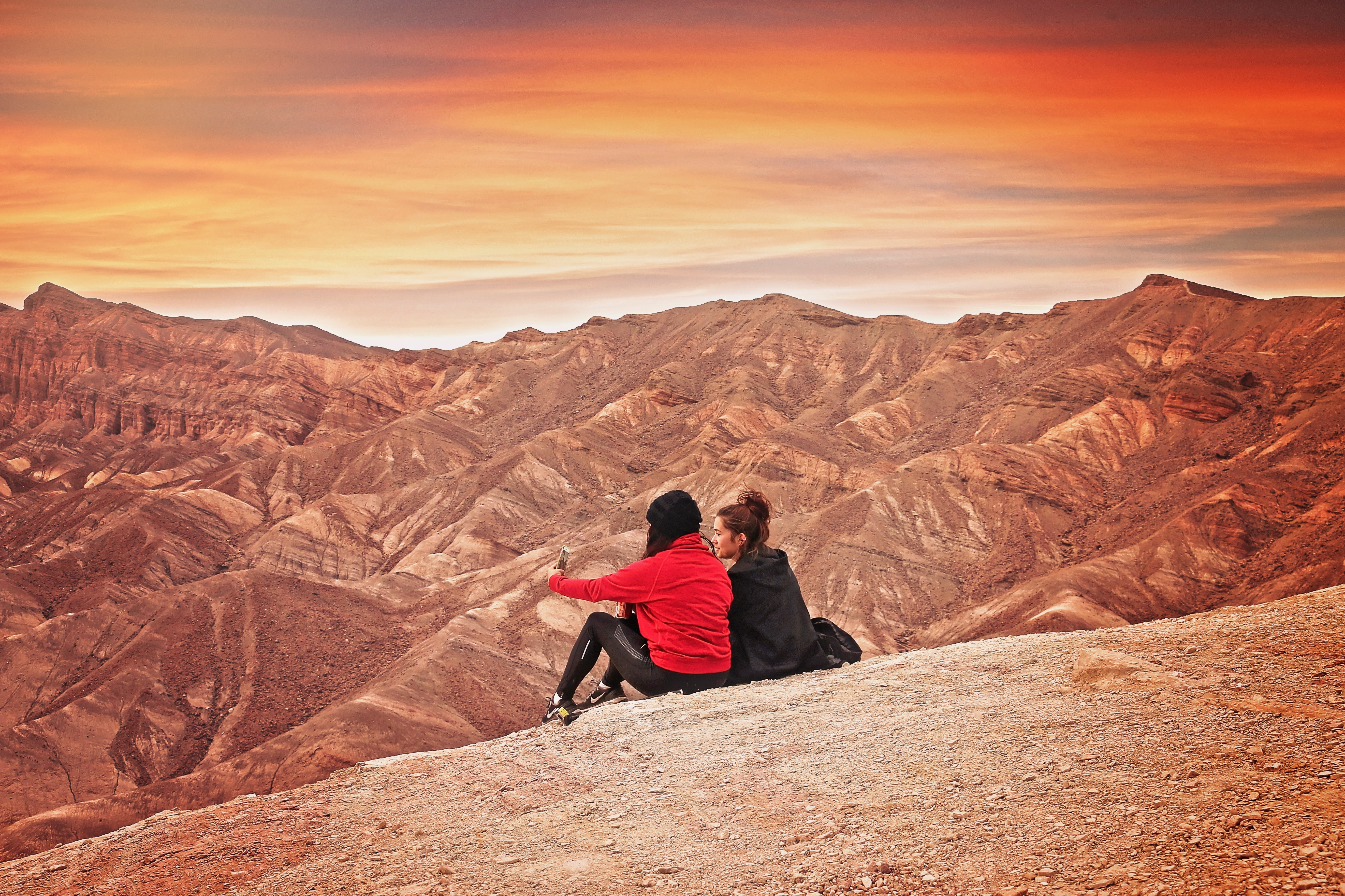 2 woman seating on the mountain cliff during golden hour photo
