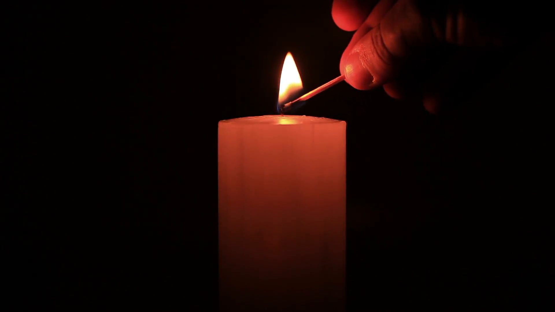 A hand with a matchstick lighting a candle in the dark (blow out at ...