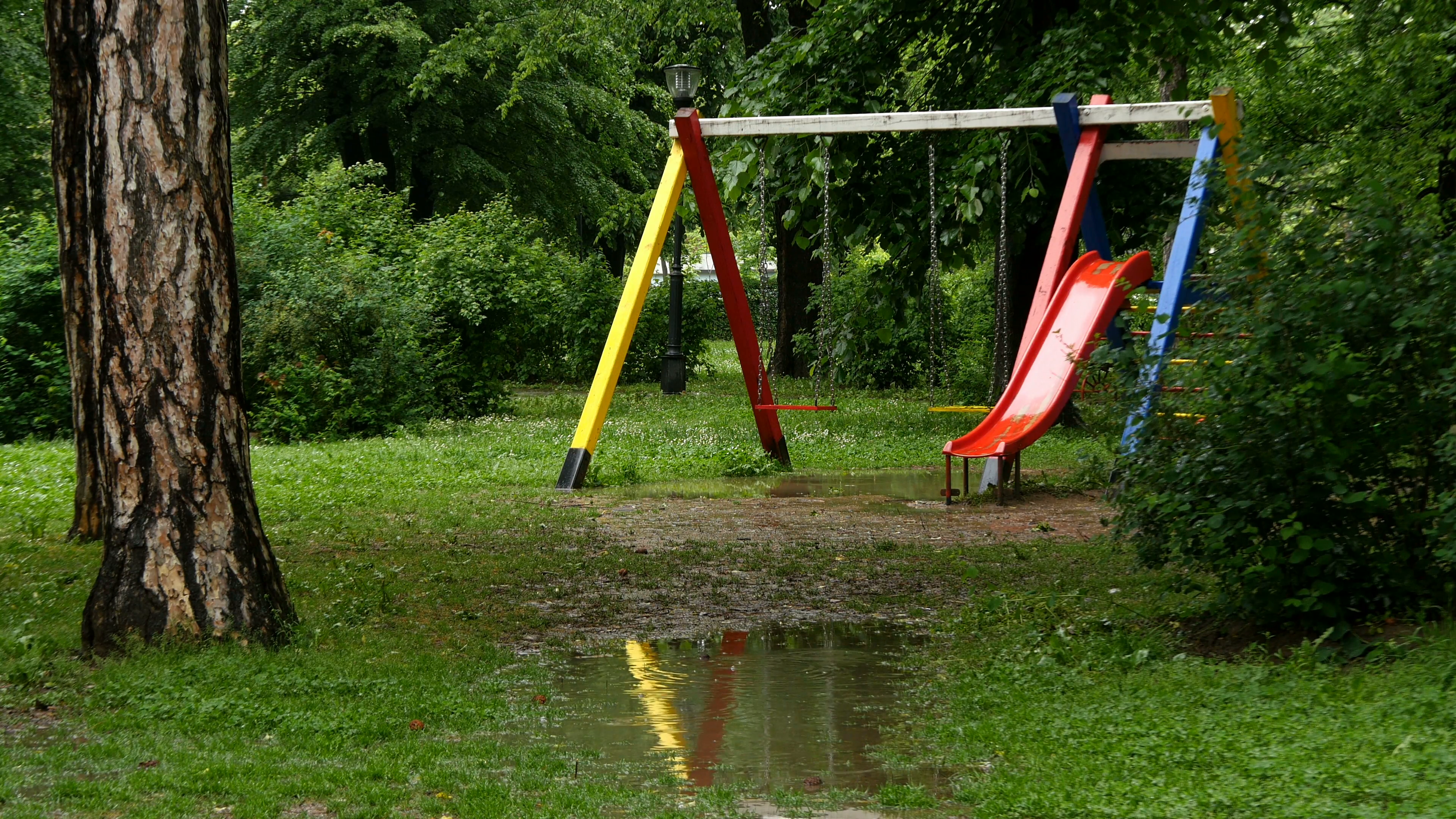 Wide shot of a swing and toboggan run in the park after the rain ...