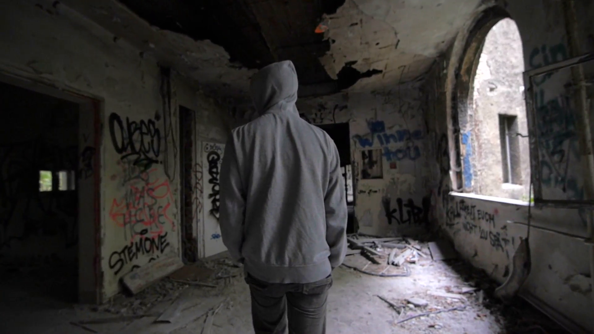 Slow motion of a guy with hood walking through abandoned building ...