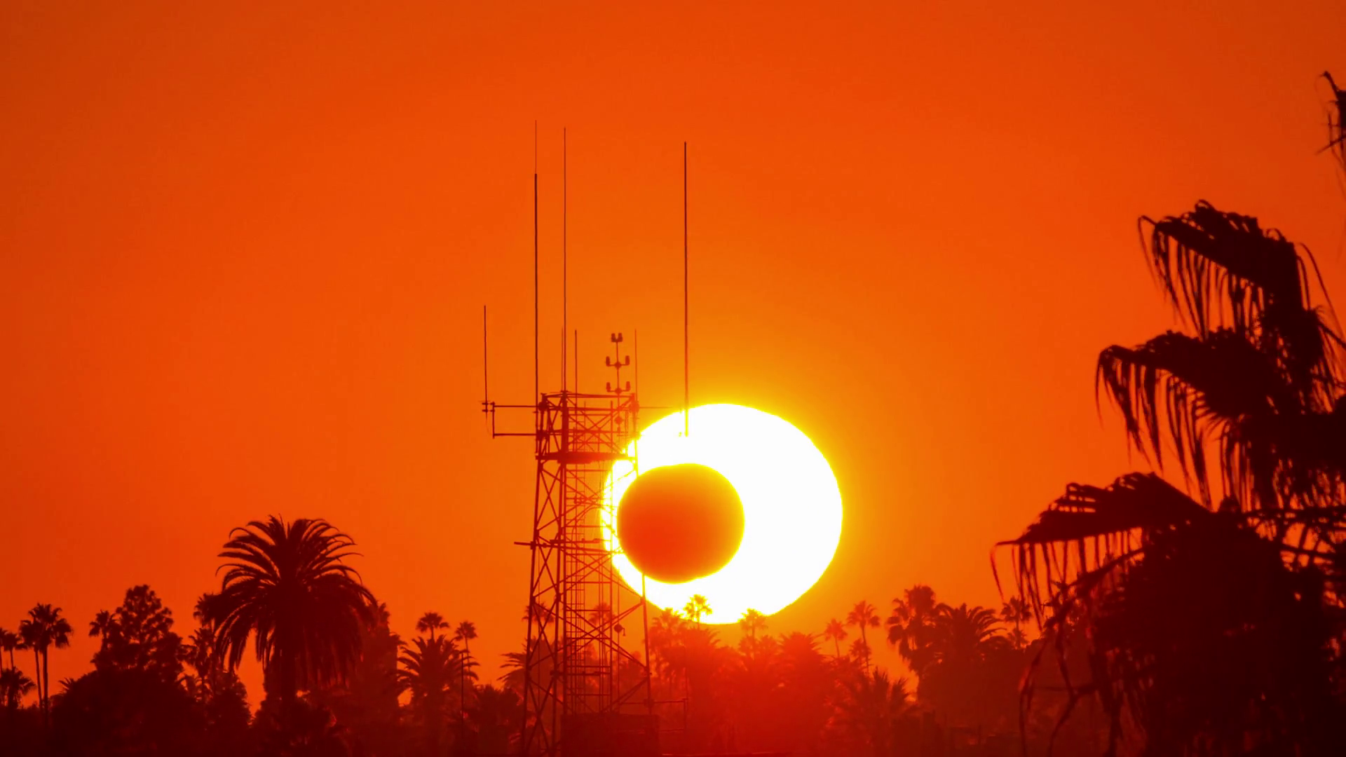 Big sun over orange sunset sky setting behind antenna tower in Los ...