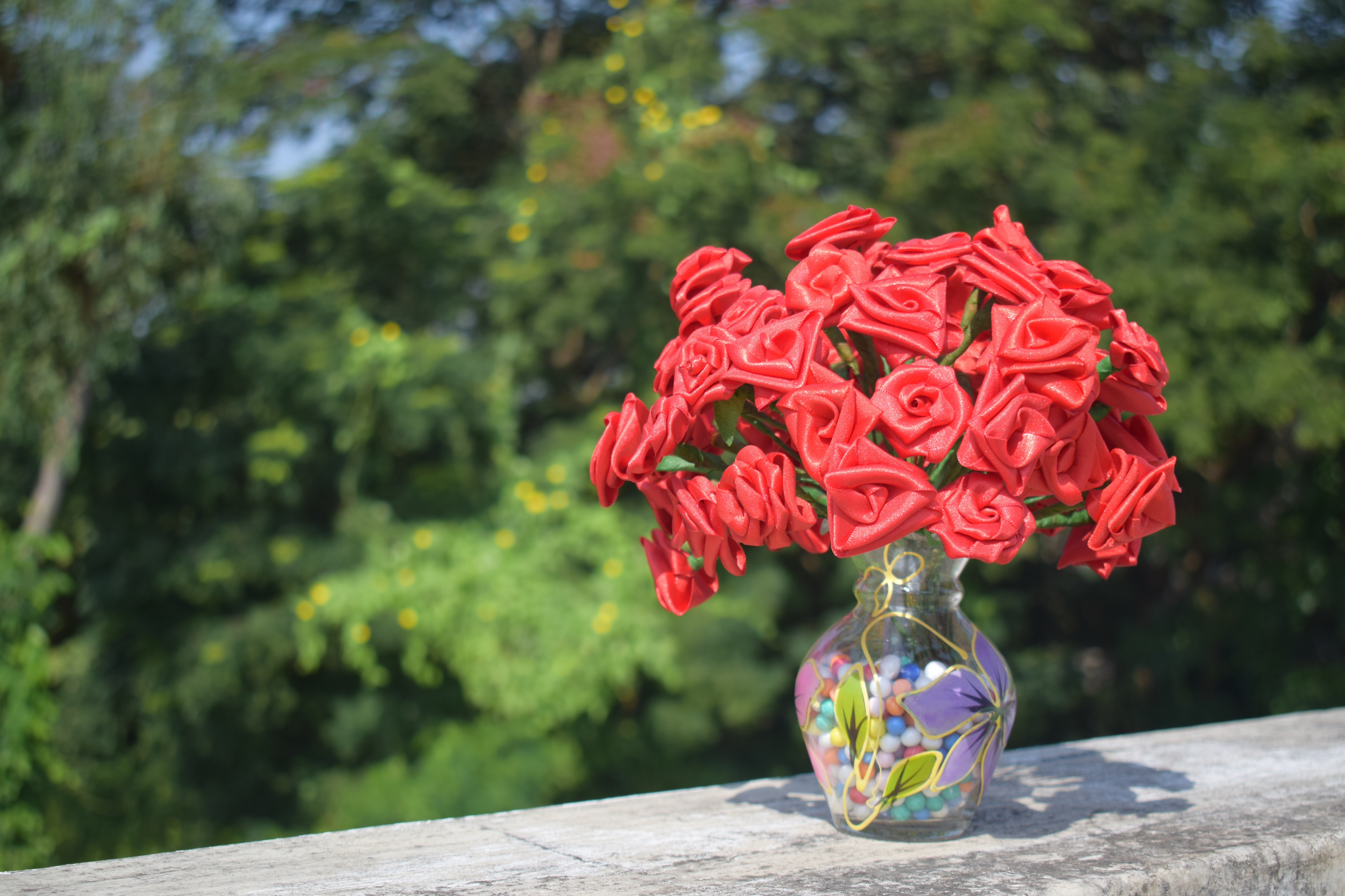 Artificial roses in clear glass vase on concrete surface photo