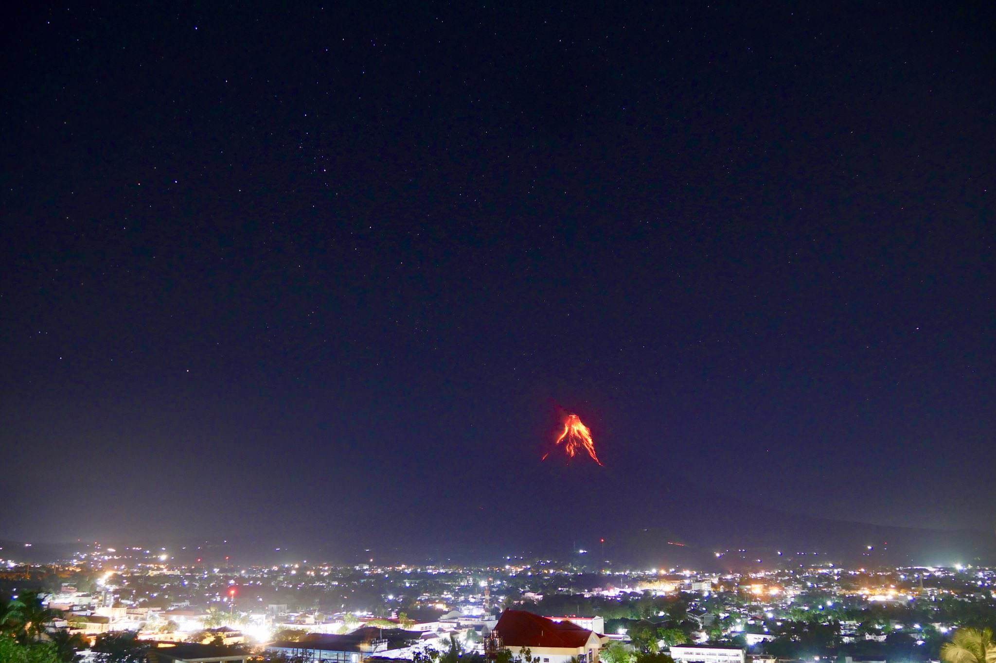 An active volcano at night nearby a town : pics