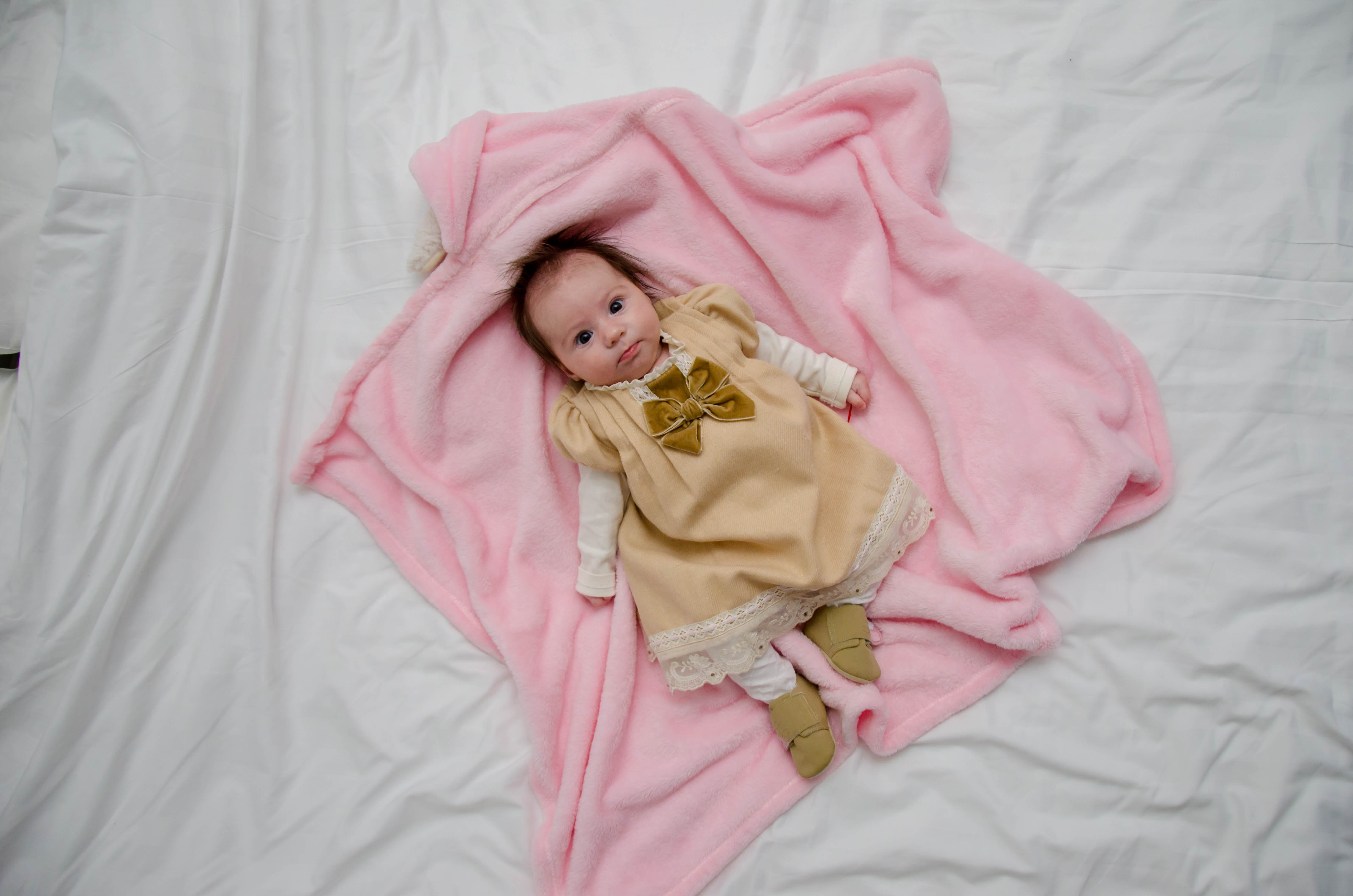 Baby in white and yellow dress on pink textile photo