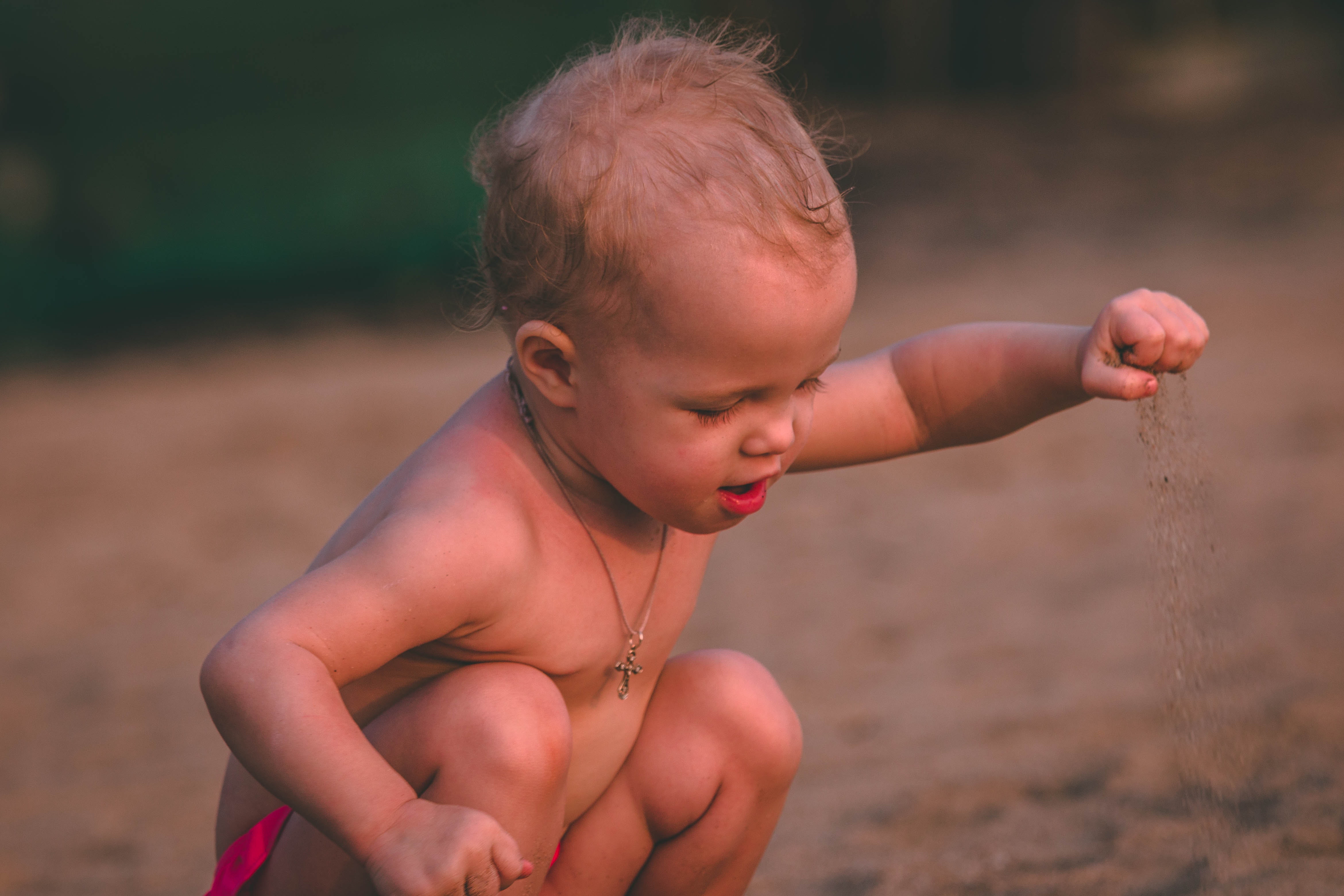 Baby with pendant necklace holding sand at daytime photo