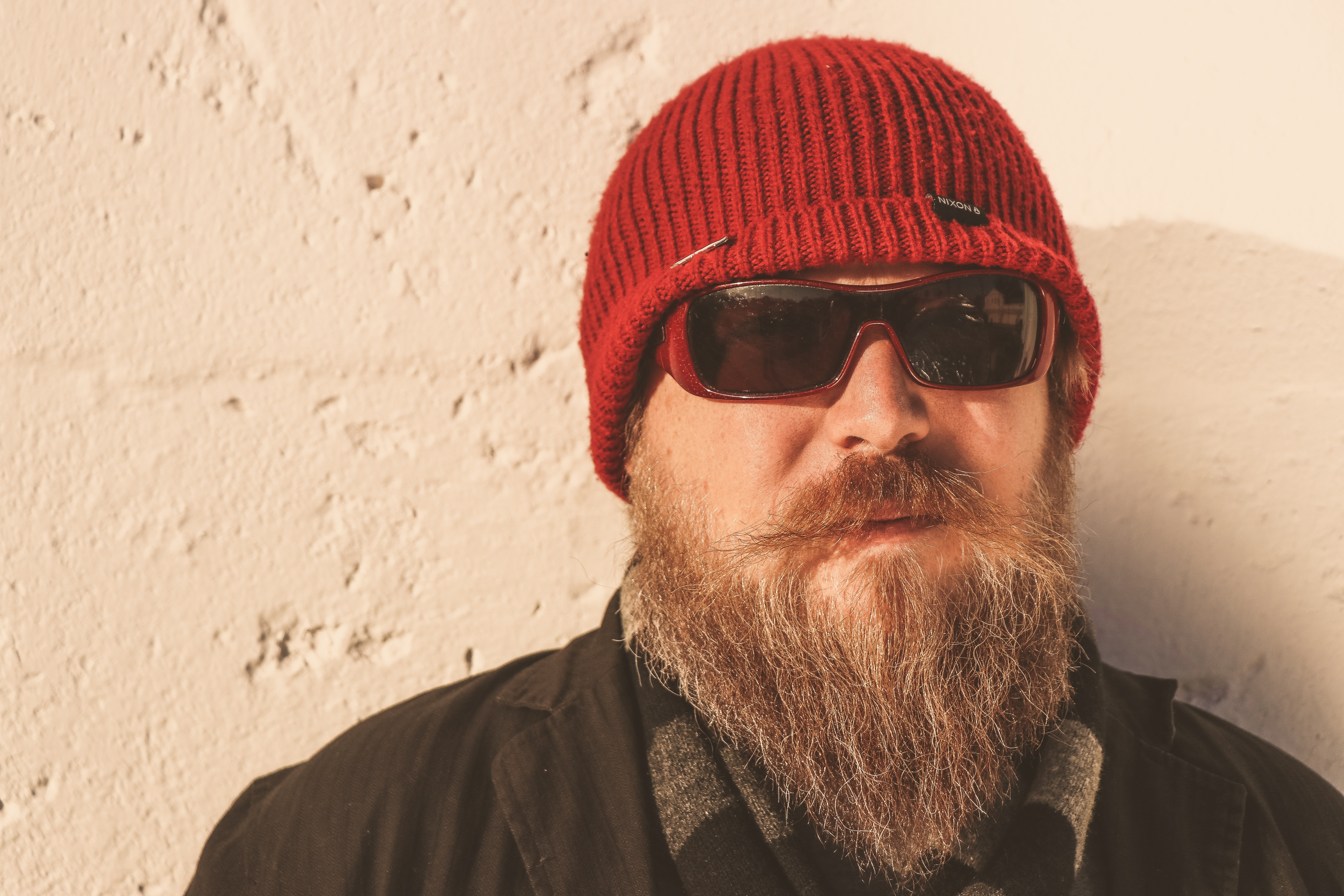 Bearded man wearing red beanie cap, sunglasses ,and black jacket photo