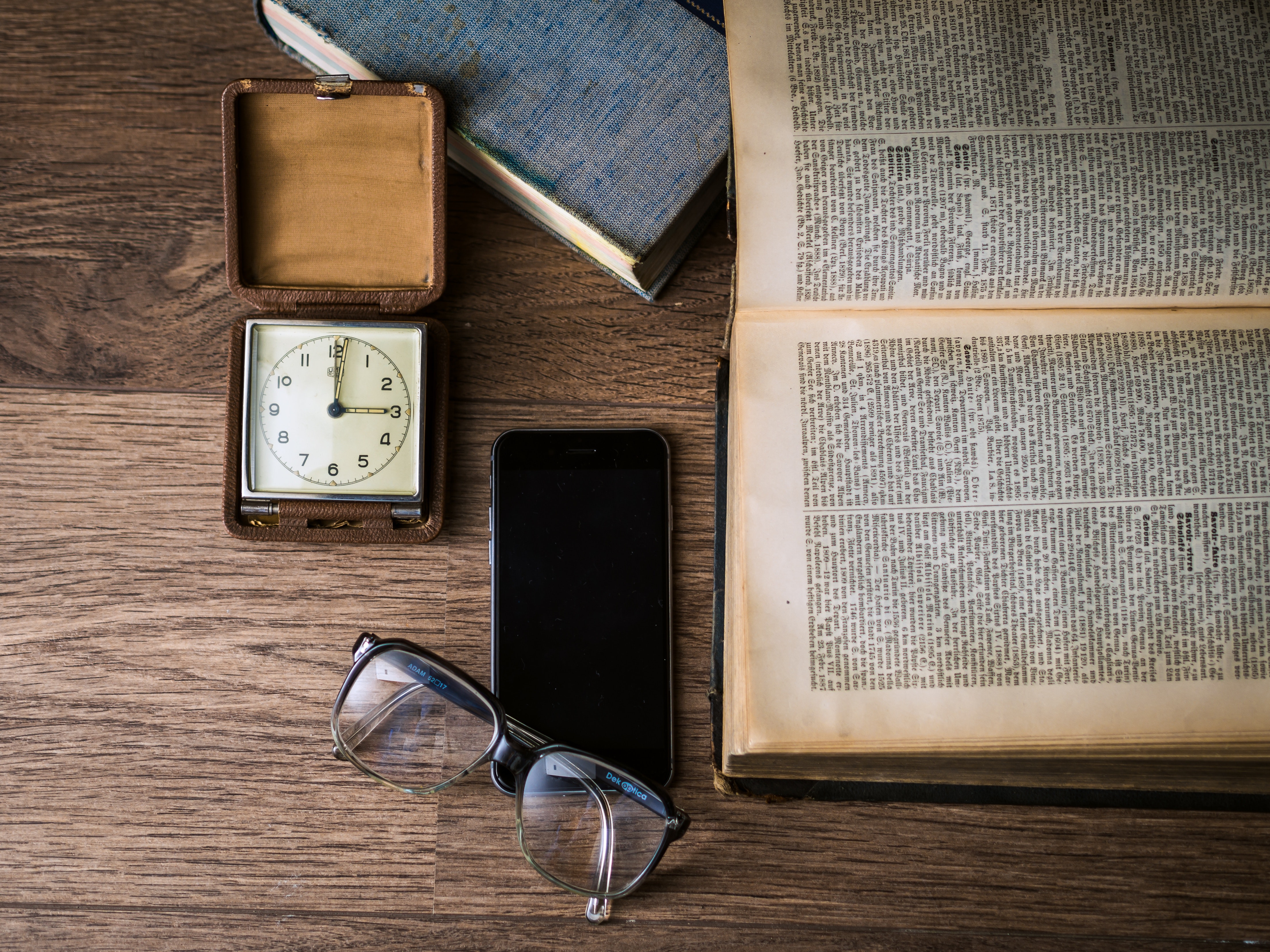 Black framed eyeglasses on top of black smartphone near brown square analog clock on brown wooden surface photo