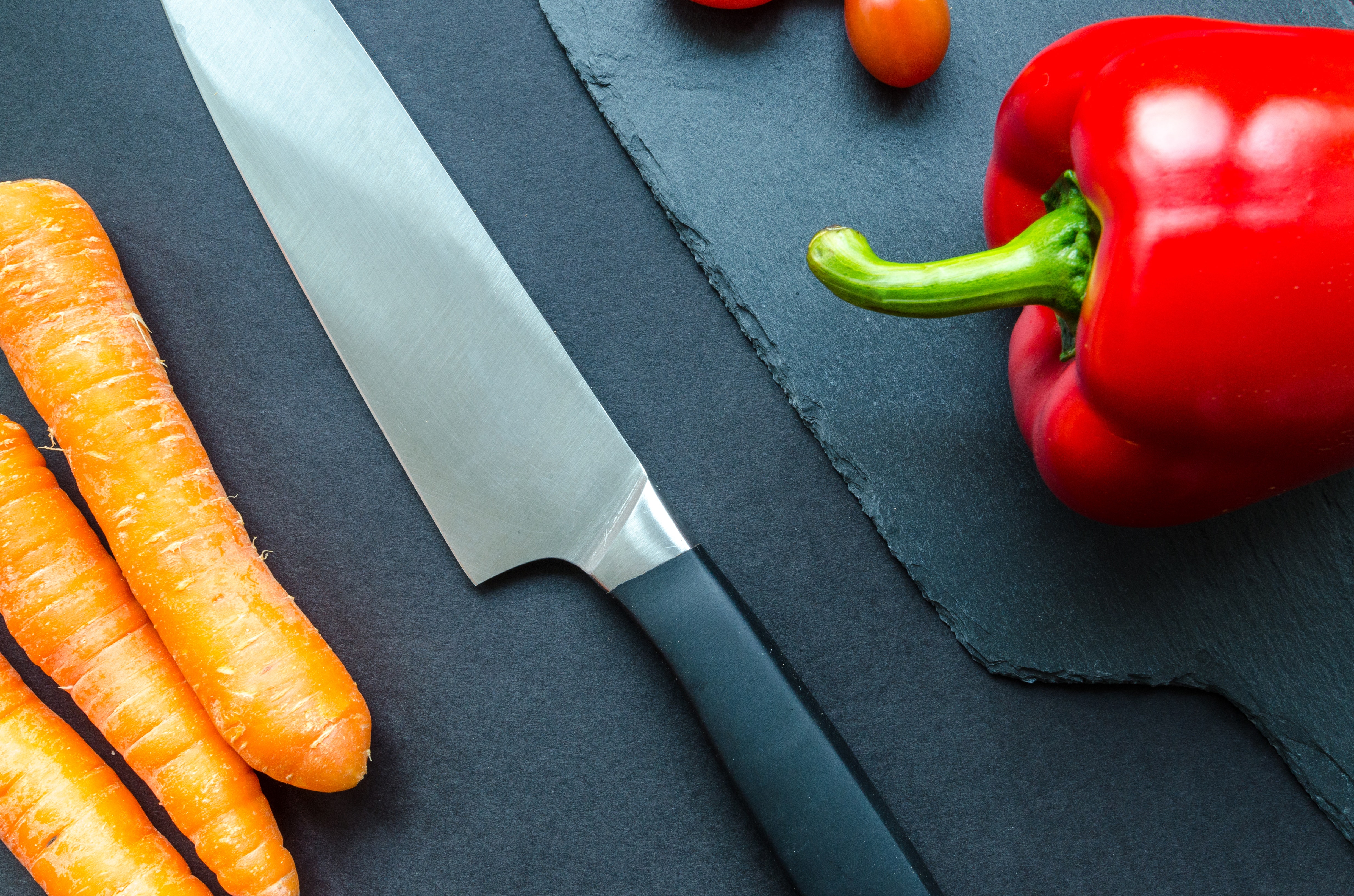 Black handled gray kitchen knife beside orange carrots and red bellpepper photo