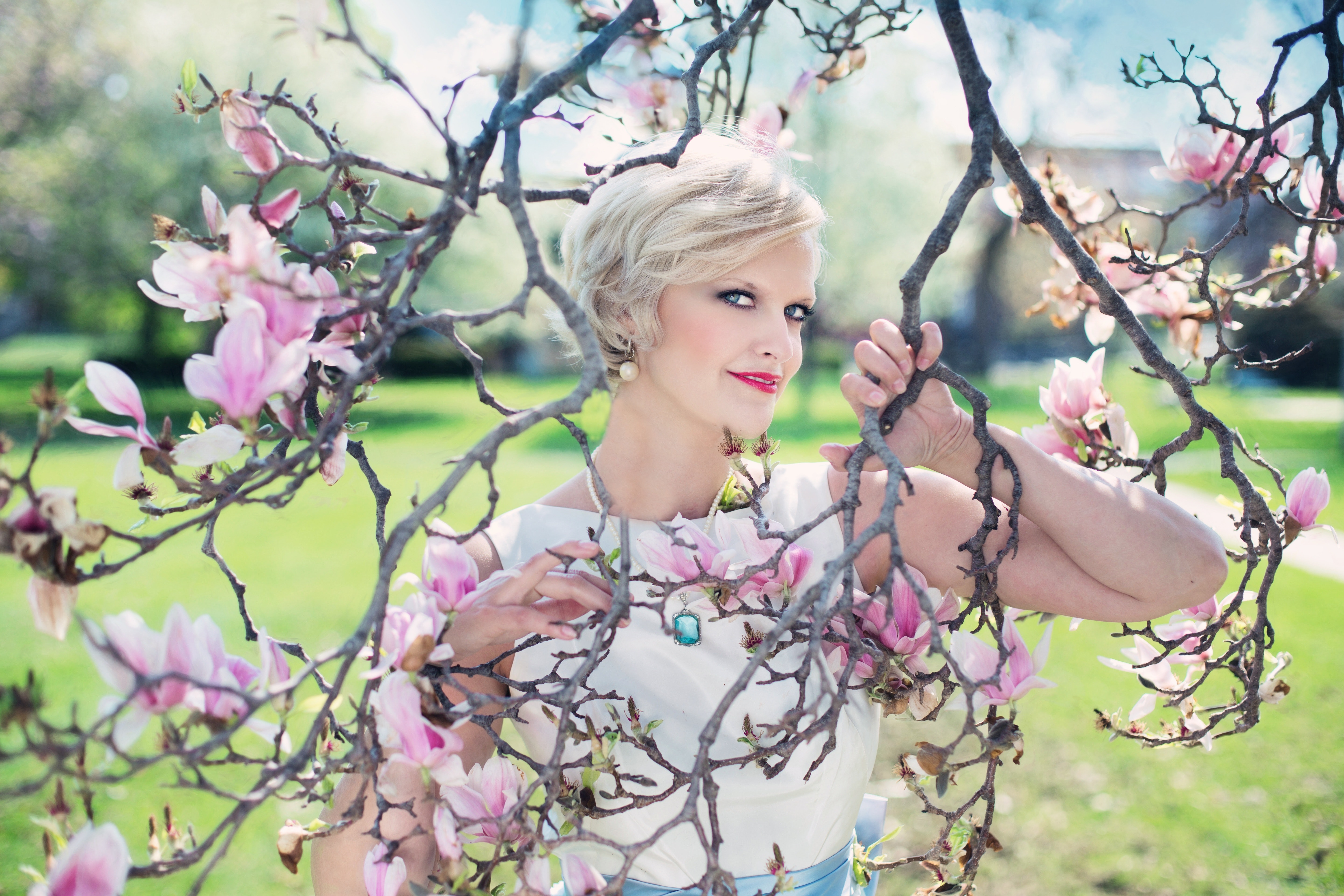 Blond haired woman posing on leafless pink flowered tree photo