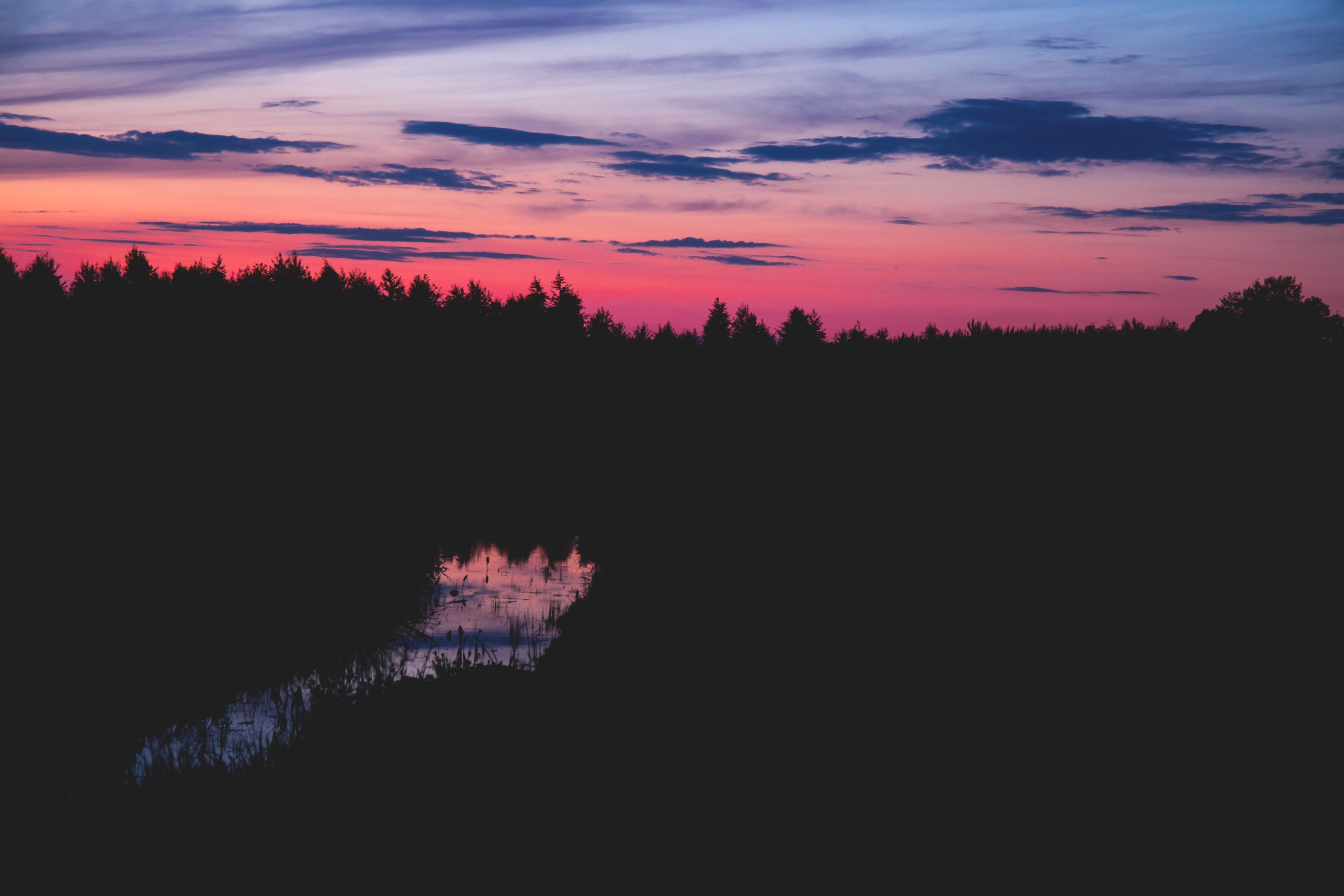 Body of water between silhouette of trees under red black and grey sky at sunset photo