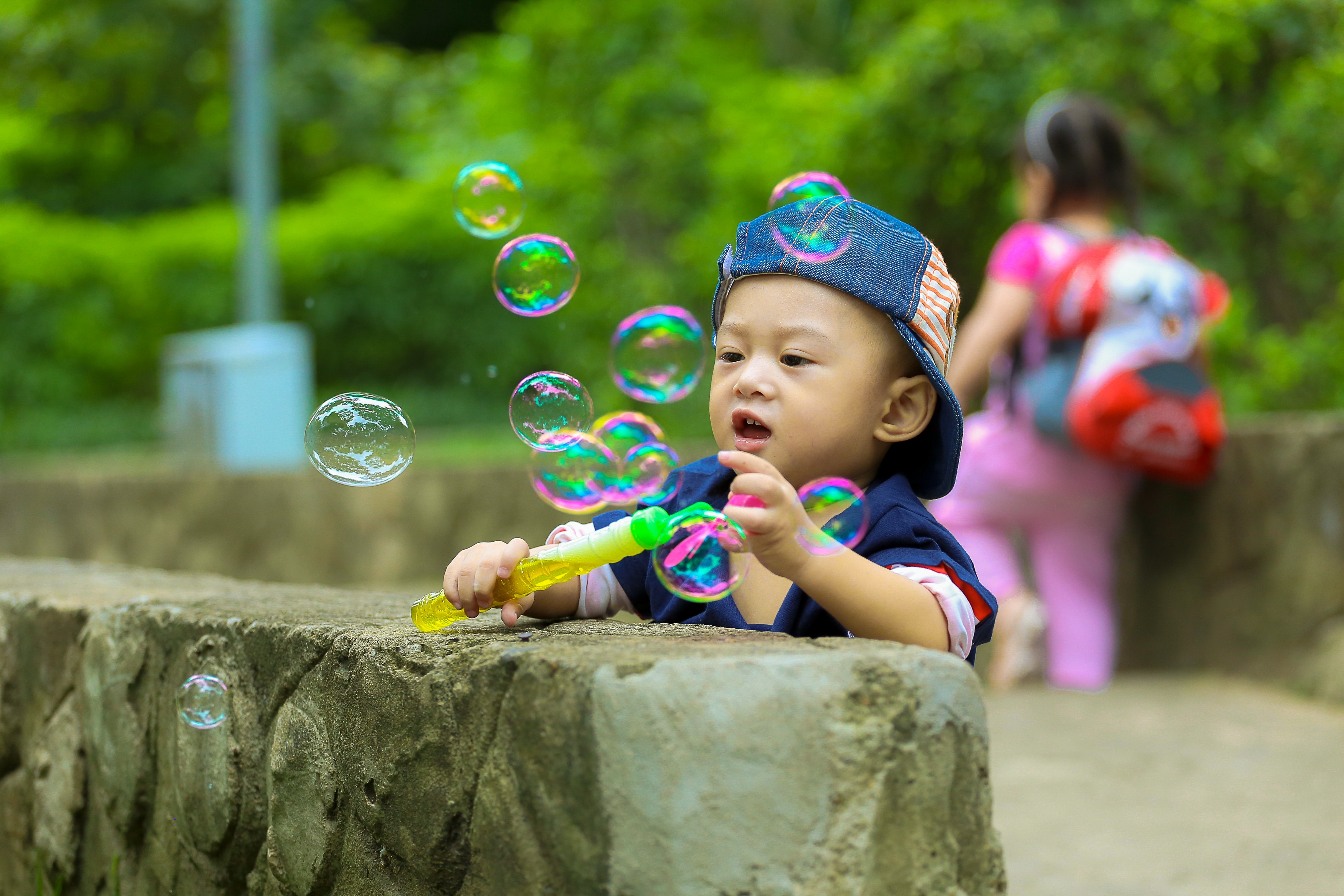 Boy in blue fitted cap playing bubbles and leaning on grey concrete wall at daytime photo