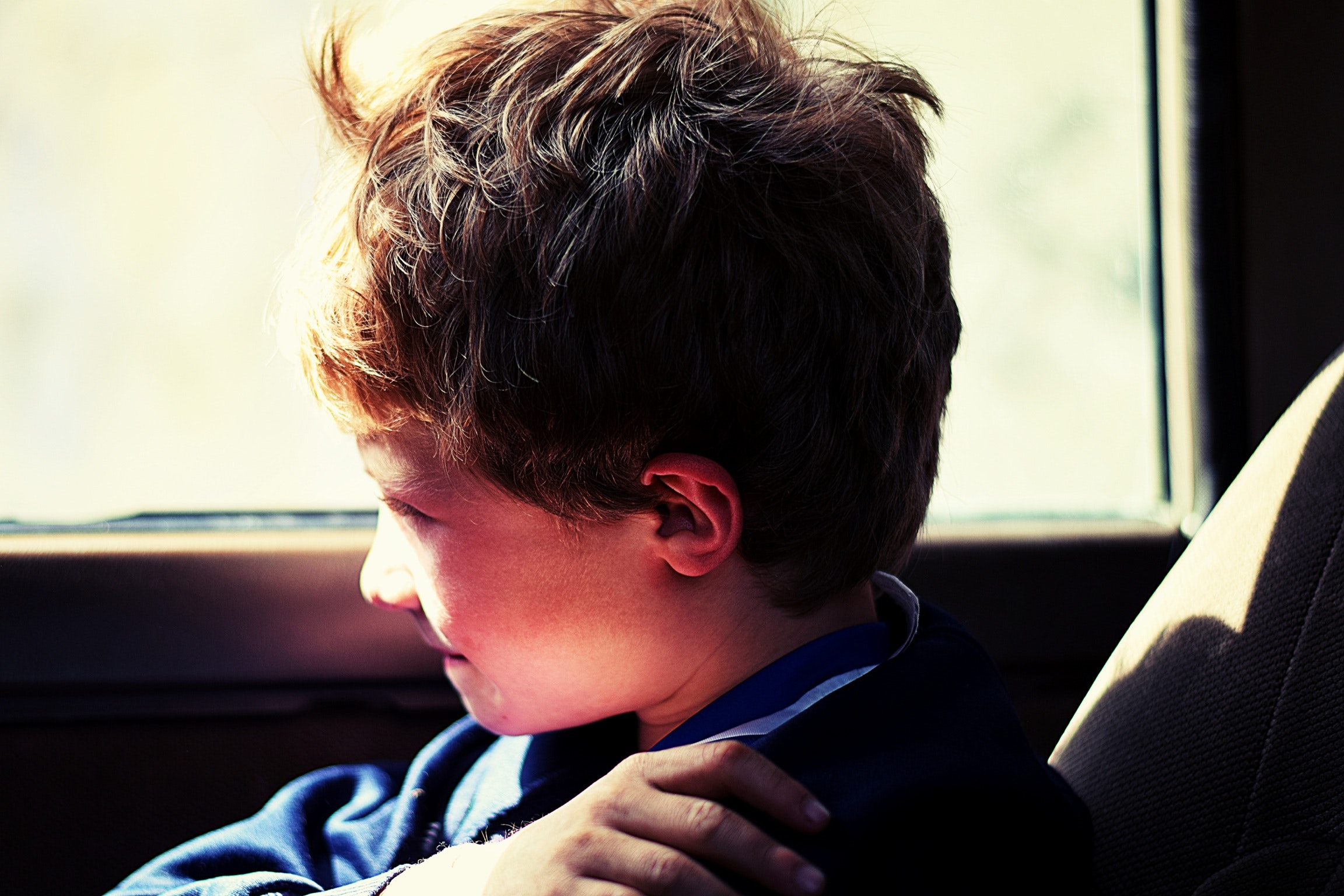 Boy in blue jacket sitting next to vehicle window photo