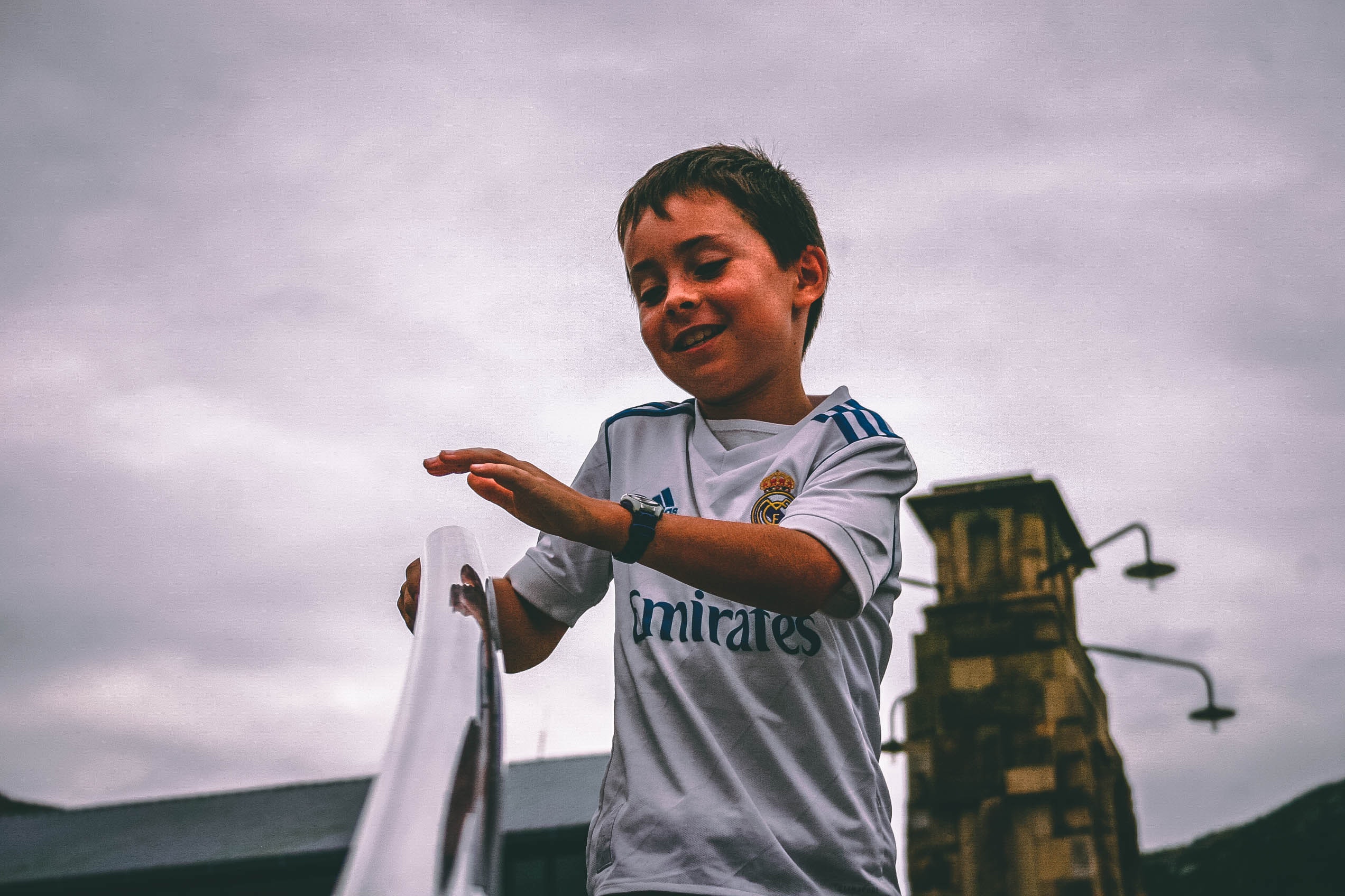 Boy in white and blue fly emirates jersey shirt holding on stairs grab bar under gray skies photo
