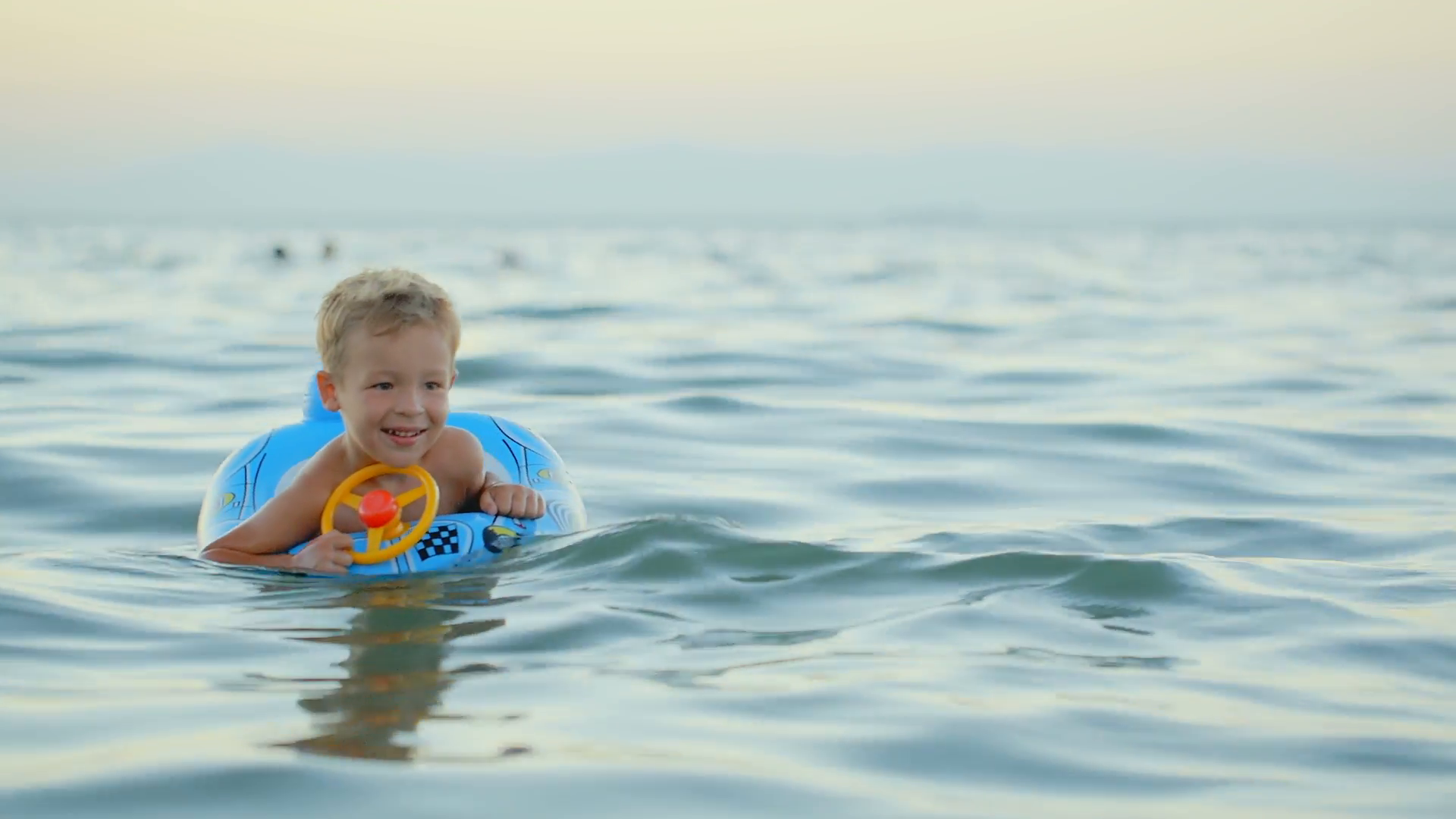 Happy little boy with rubber ring made as car swimming in sea ...