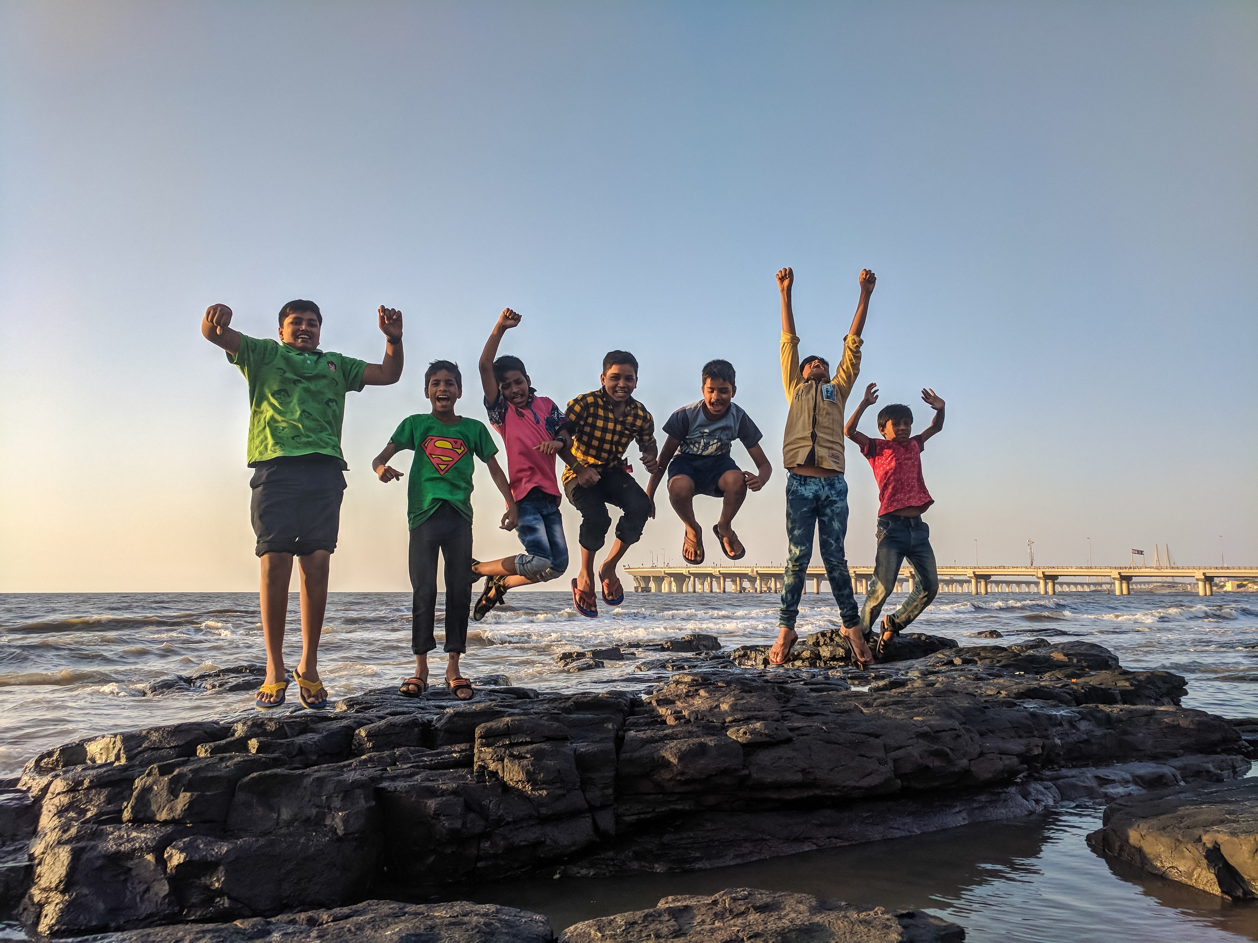 Boy wearing green crew-neck shirt jumping from black stone on seashore photo