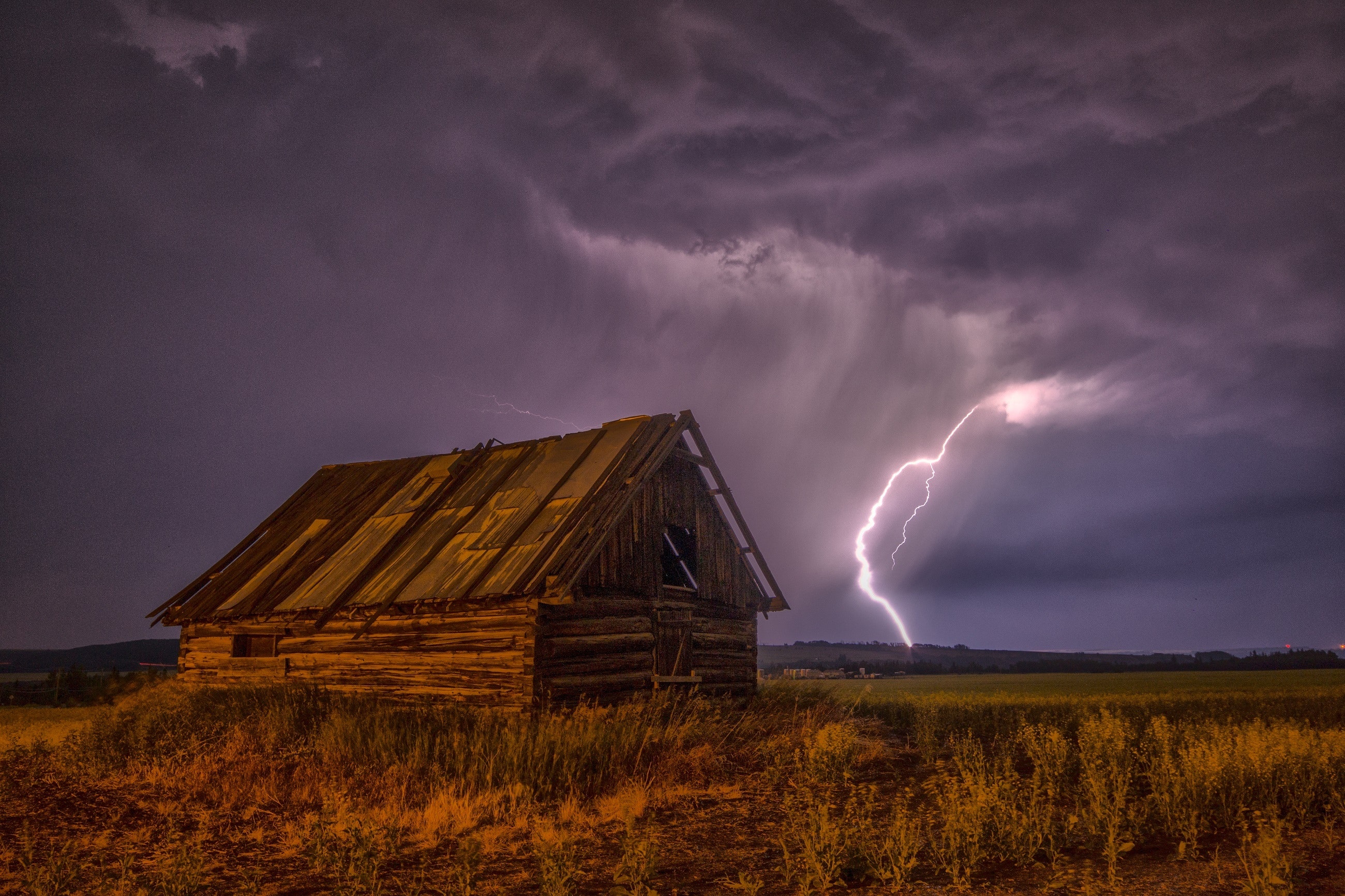 Brown and beige wooden barn surrounded with brown grasses under thunderclouds photo