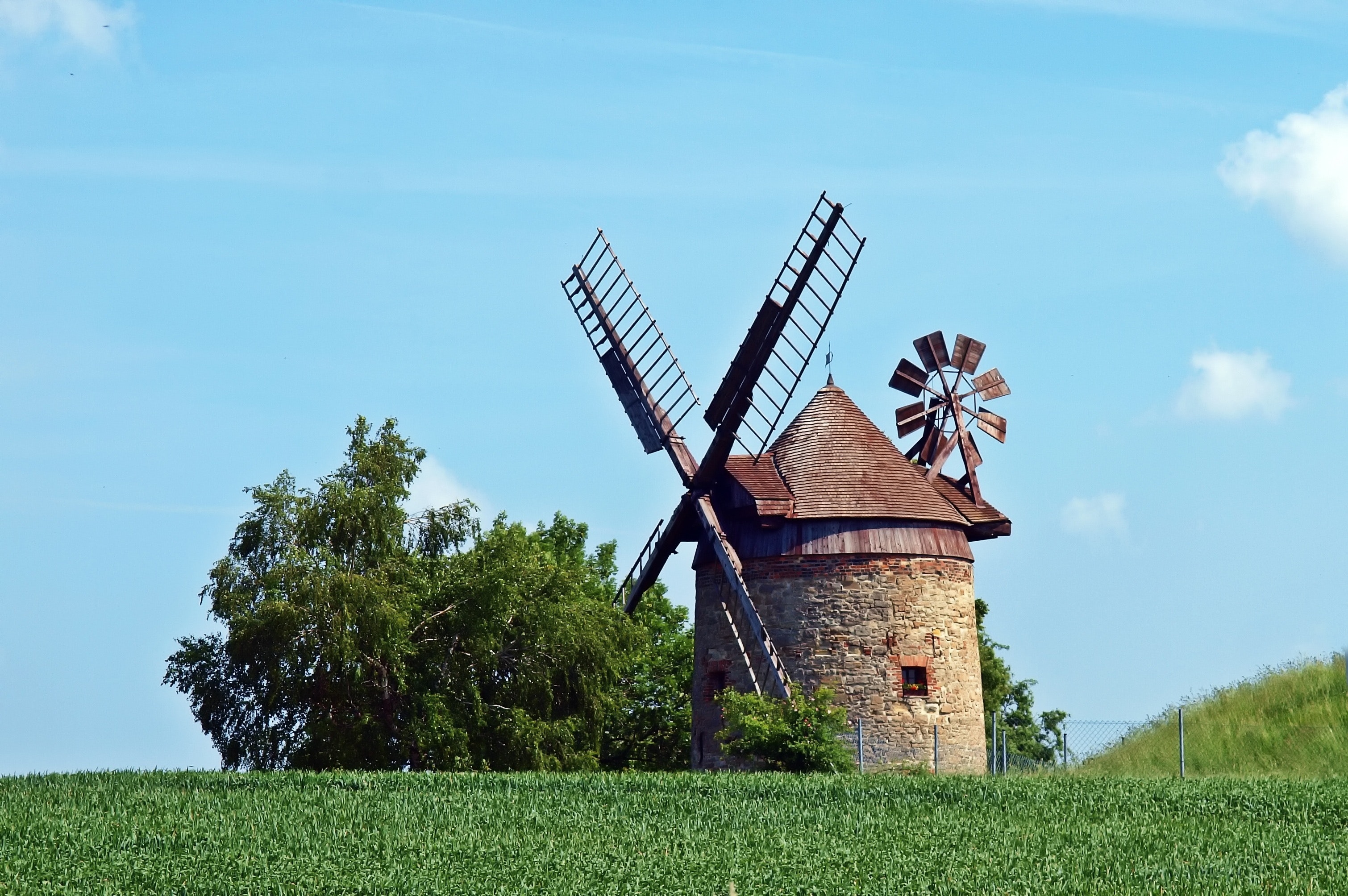 Brown and gray windmill beside green tree under blue cloudy sky during day time photo