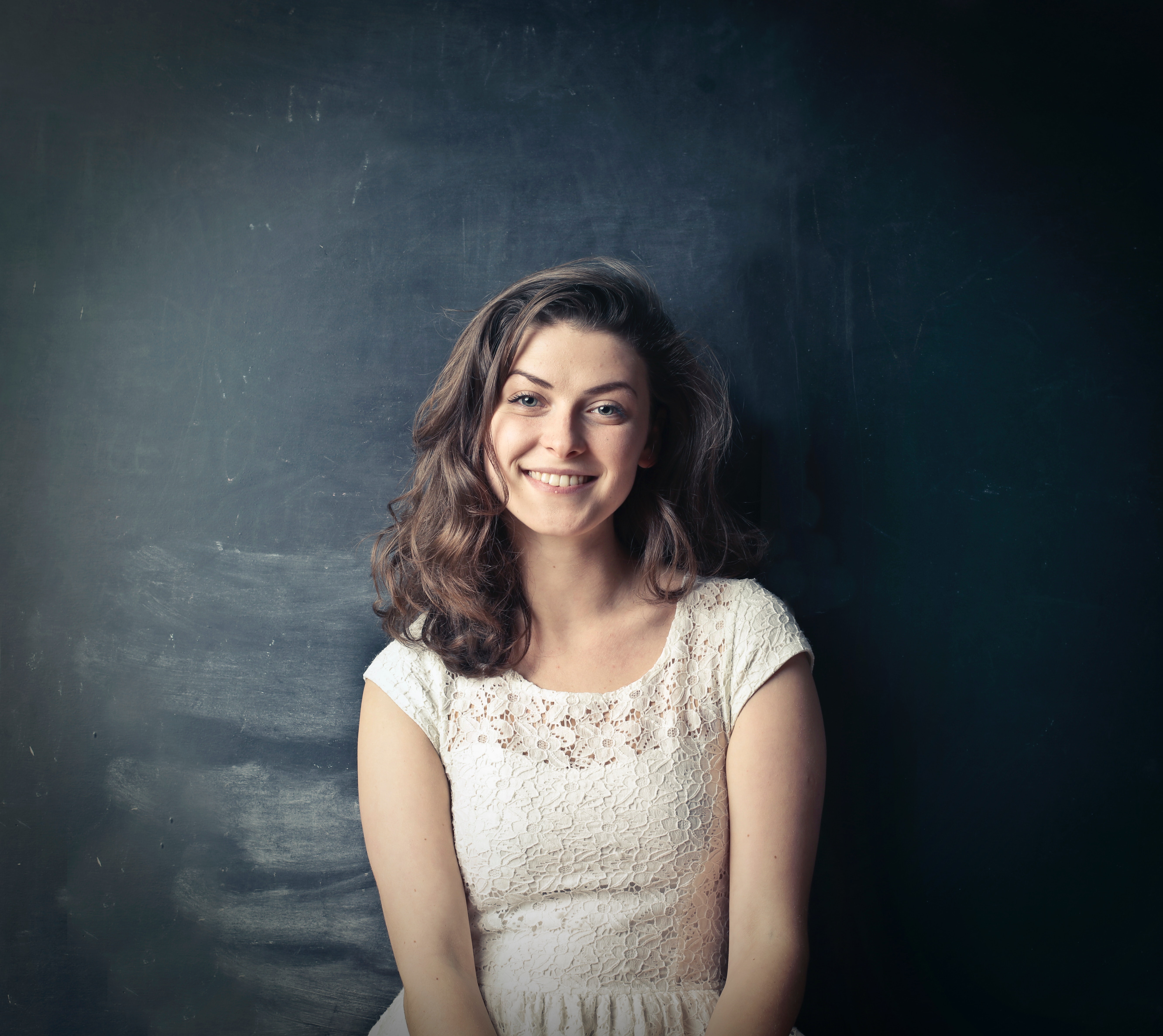 Brown haired girl in white sleeveless dress standing beside black painted wall photo