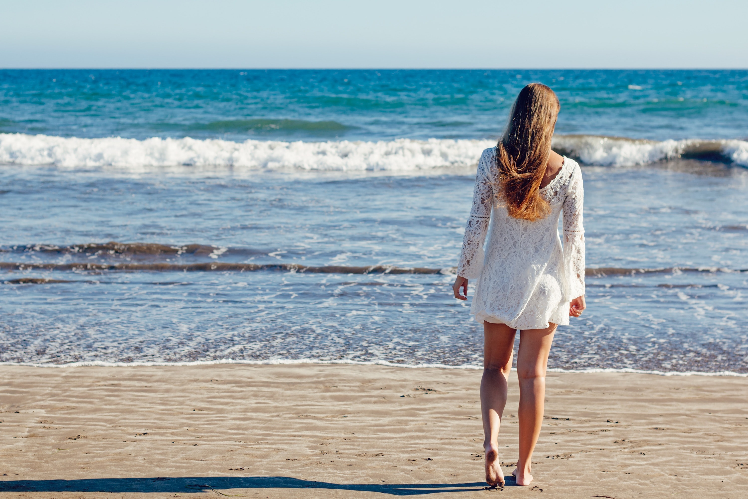 Brown haired woman in white lace long sleeve mini dress standing on seashore photo