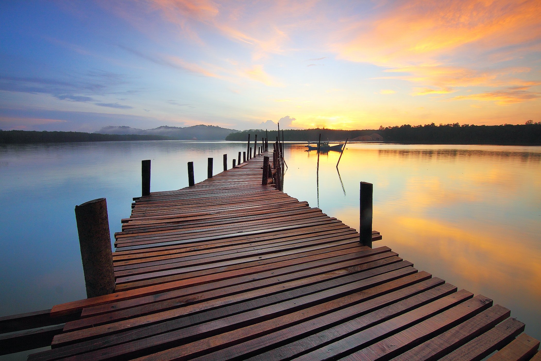 Brown wooden dock on calm body of water surrounded by silhouette of trees during sunset photo