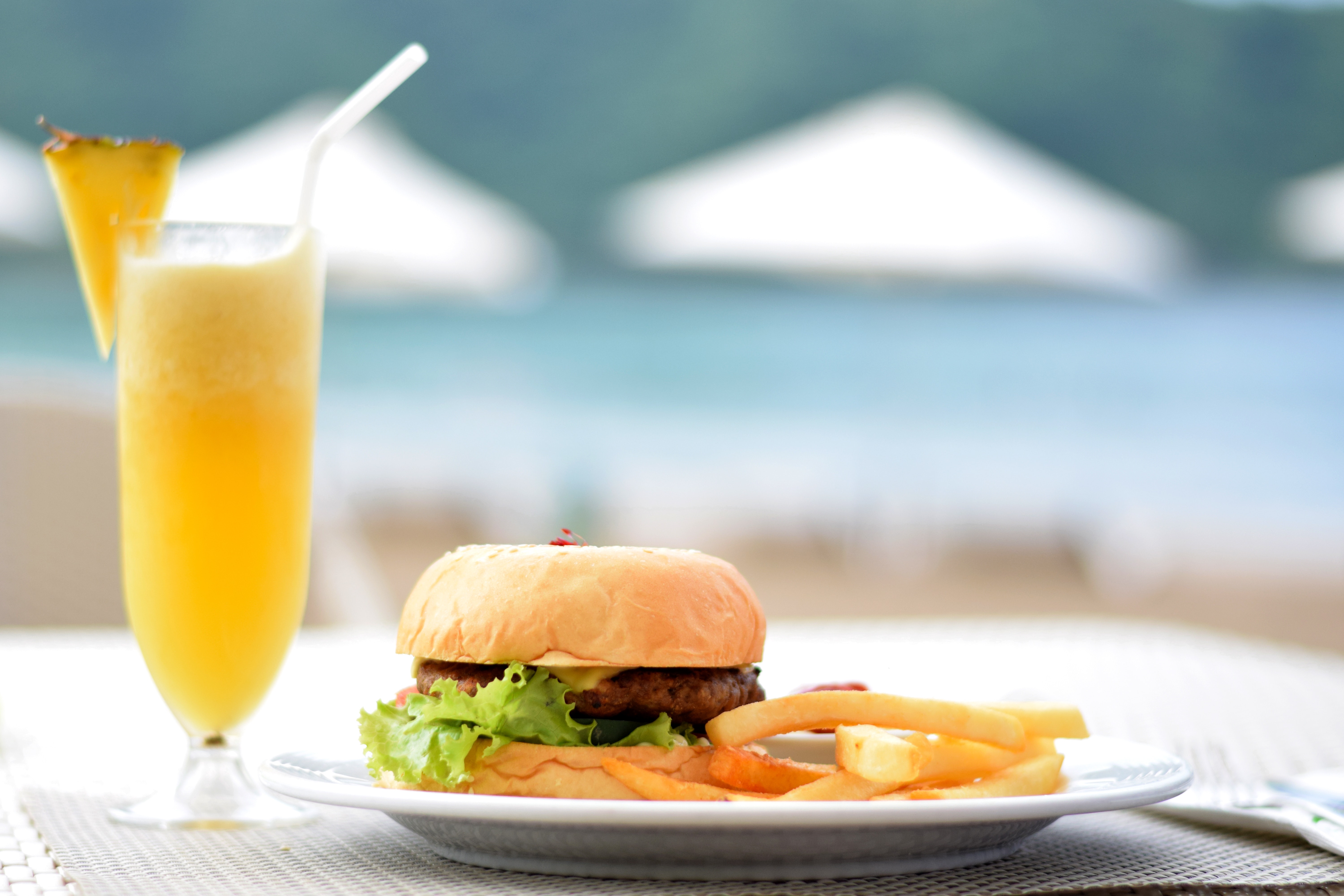 Burger with lettuce and fries on plate beside pineapple juice photo