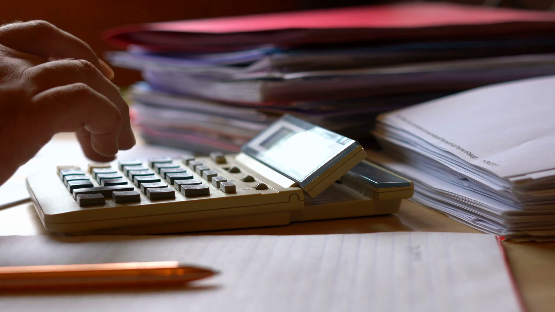 Accountant using calculator with stacks of paperwork and filing, in ...