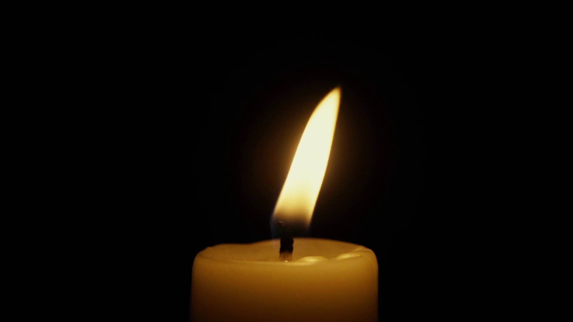 Candle flame gently swaying in the wind on a black background near ...