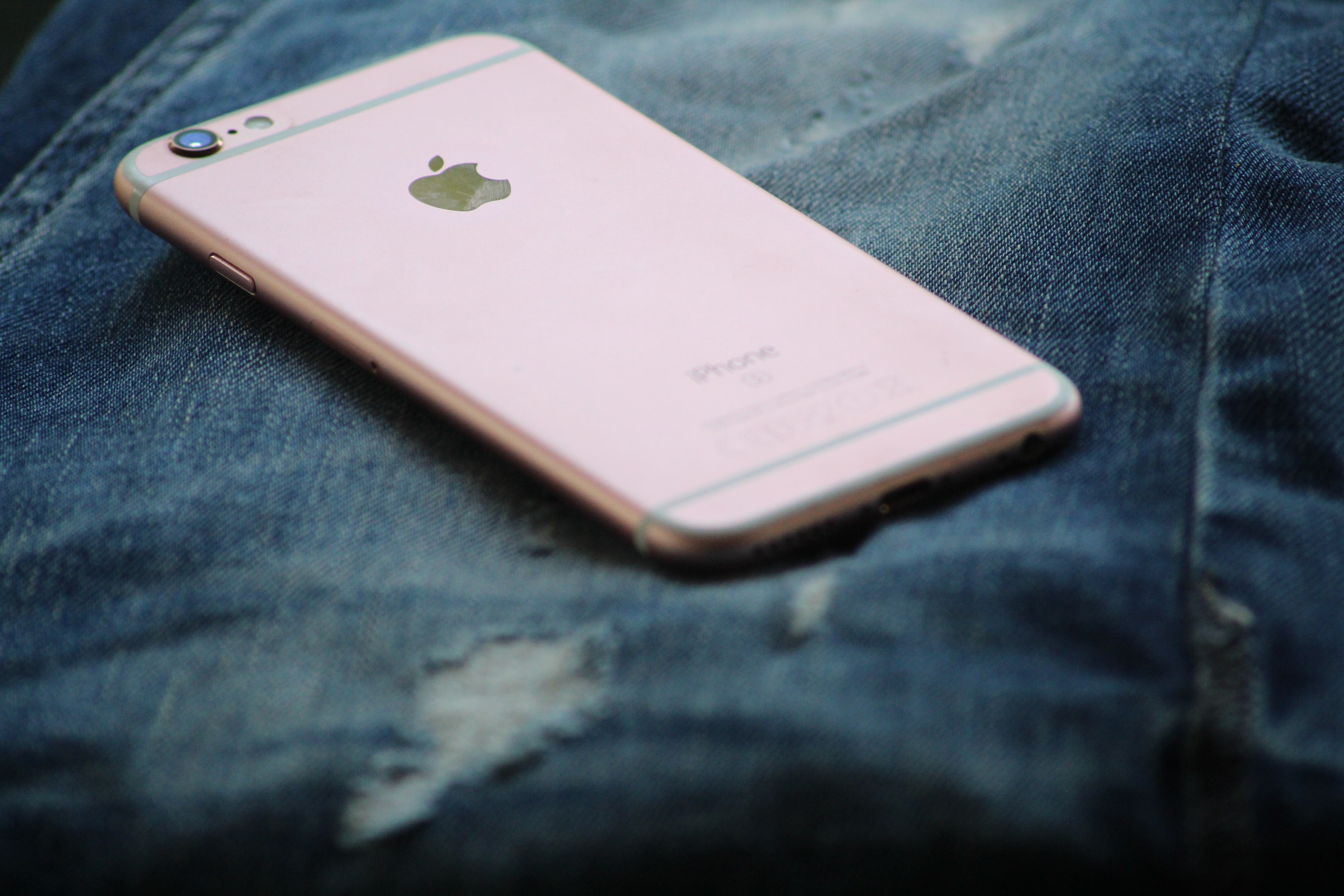 Close-up photography of rose gold iphone 6s on top of blue denim jeans