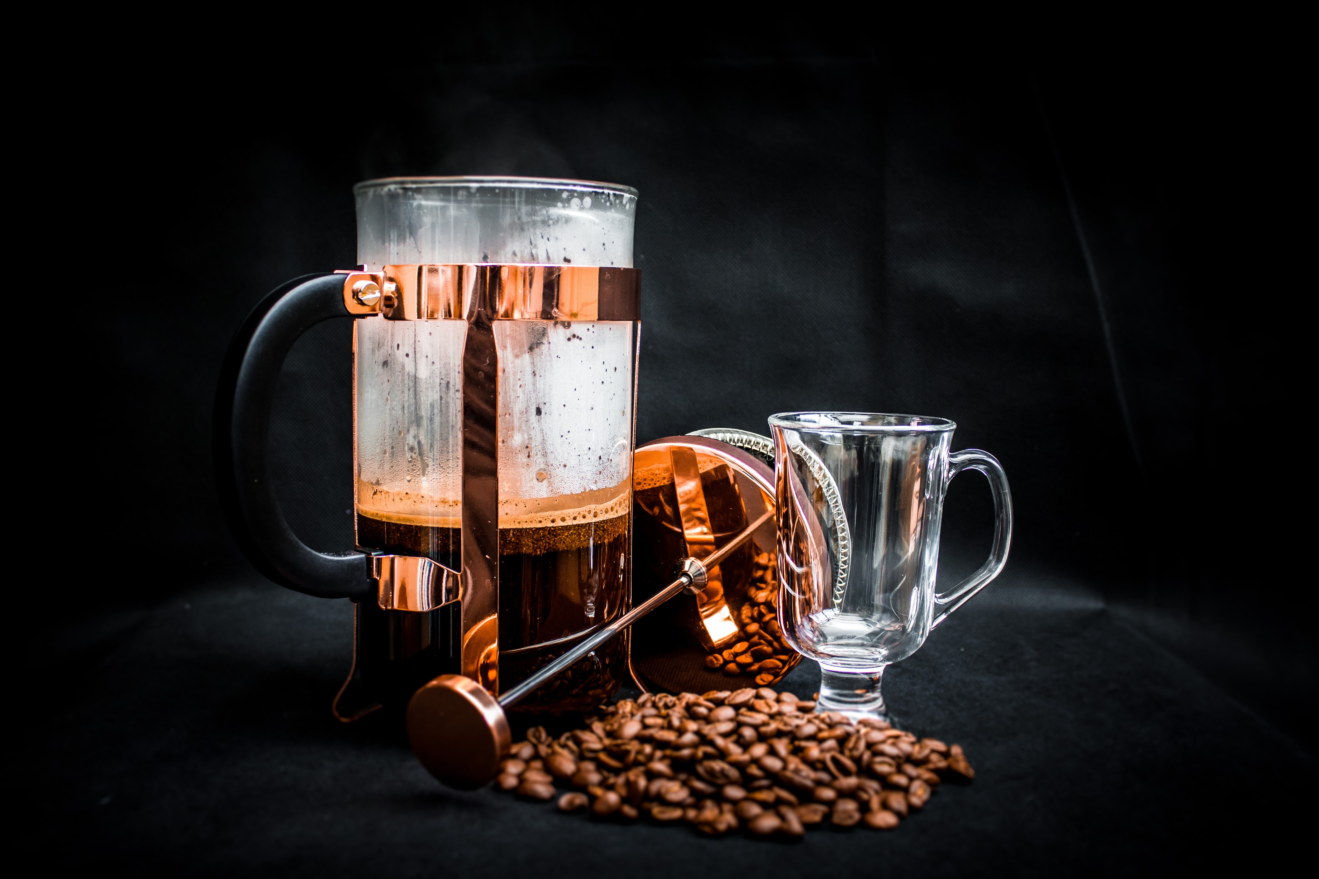Coffee beans beside coffee press and glass cup photo