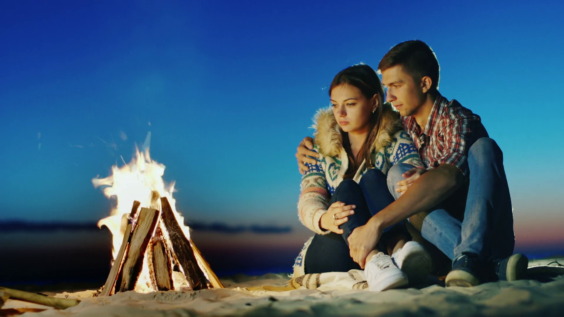 Romantic young couple sitting on the beach campfire. Hug, admiring ...
