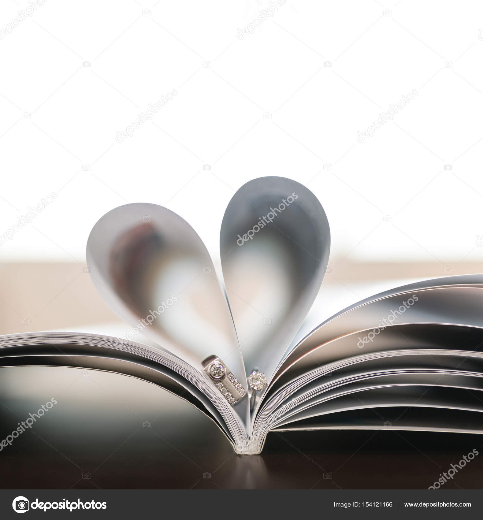 Pages of book curved into heart shape with couple wedding rings ...