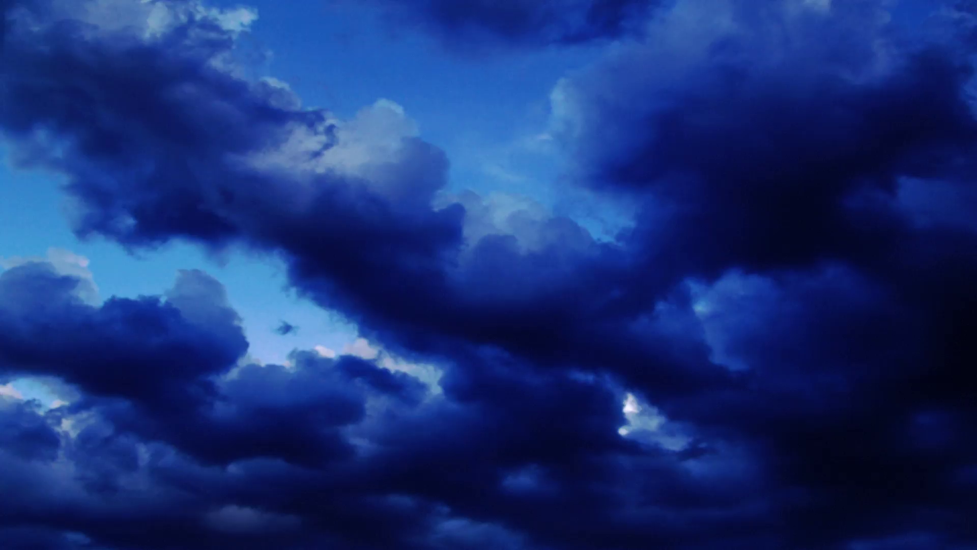 Dark clouds in a deep blue sky roll left across the sky. Stock Video ...