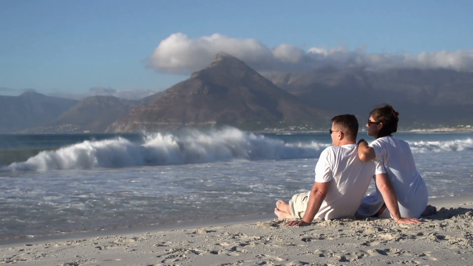 Couple sitting close together on beach and enjoying the view, Cape ...