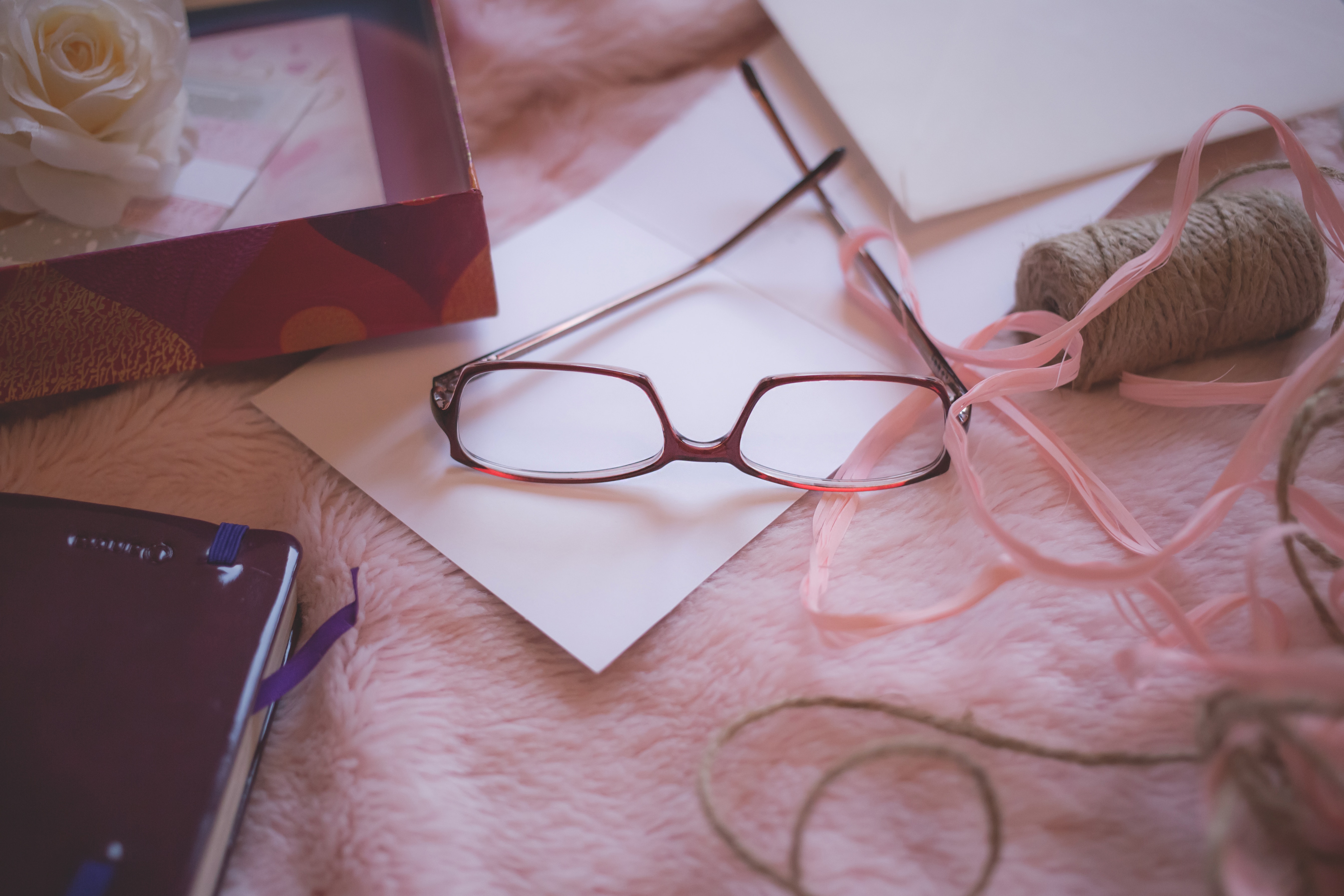 Eyeglasses beside pink yarn on pink bed blanket photo