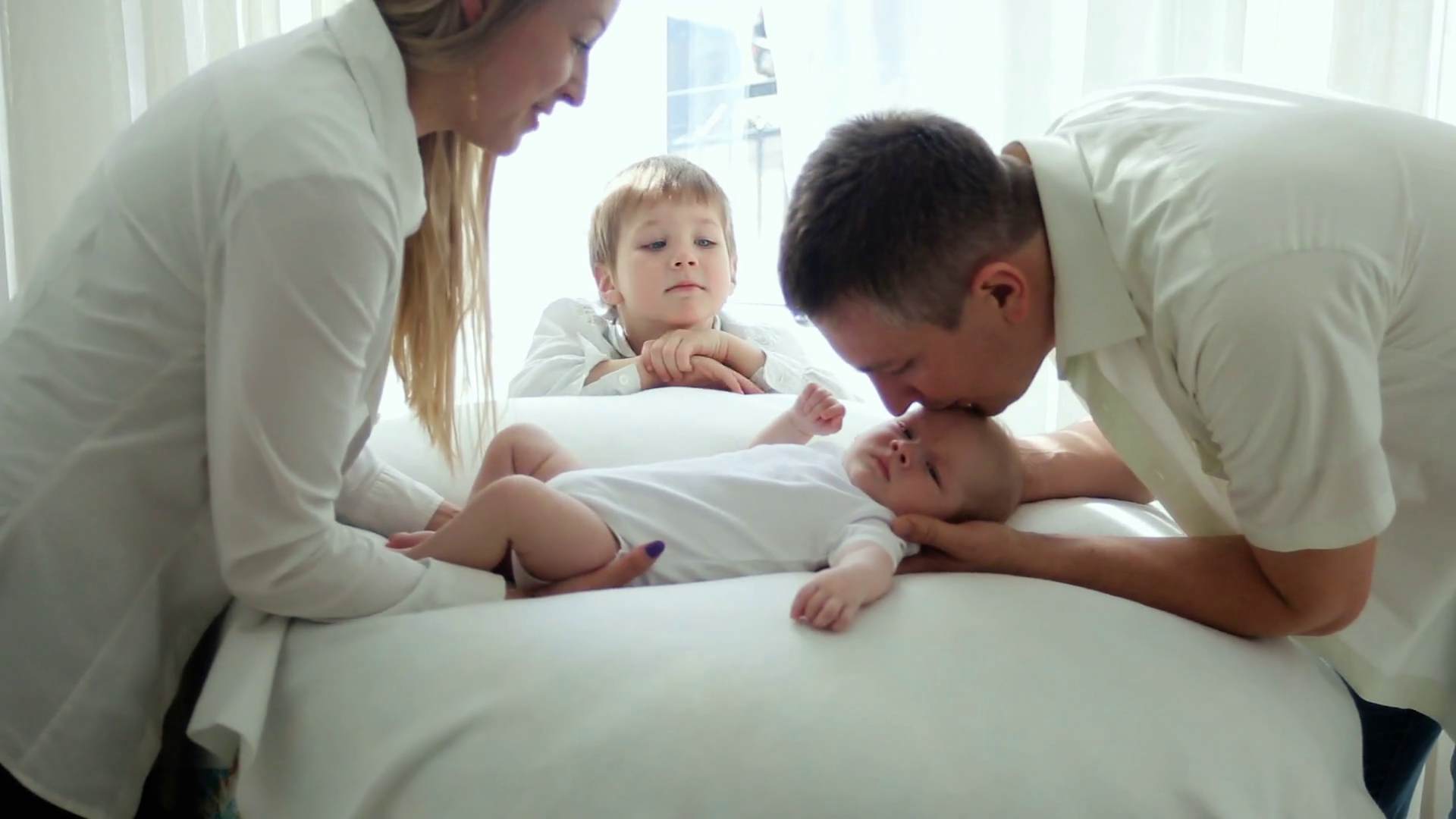 parents mother and father kiss newborn son lying on the bed and ...