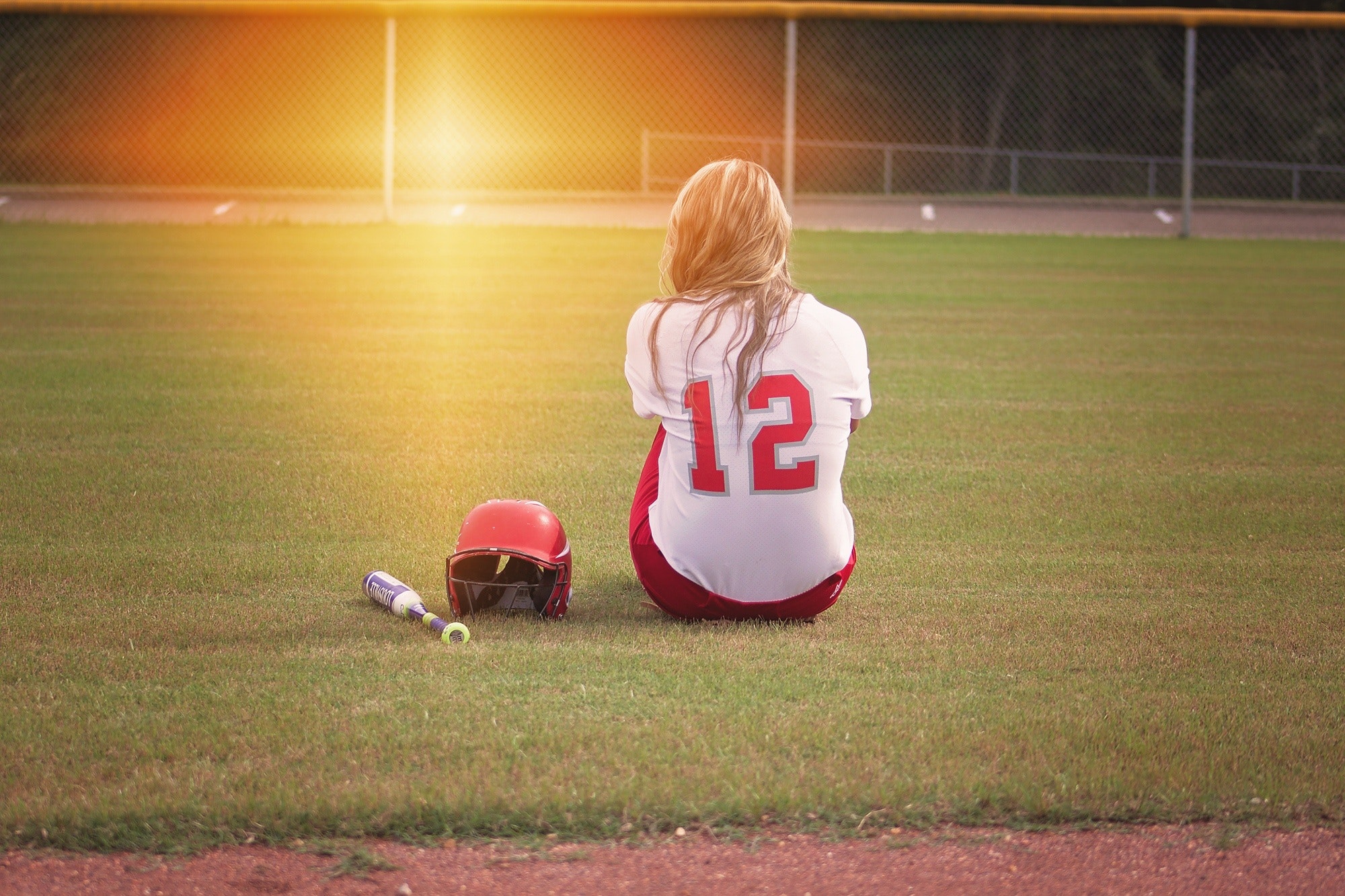 Female baseball player sitting on grass field beside helmet and baseball bat photo