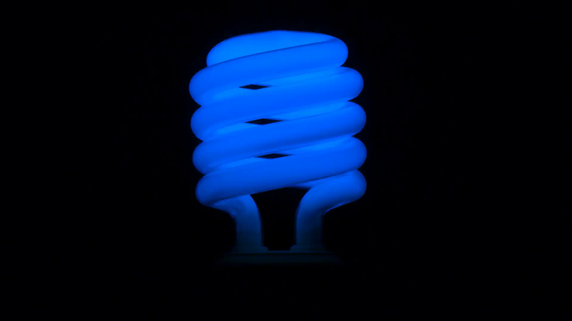 Flickering blue fluorescent light bulb in dark room against black ...