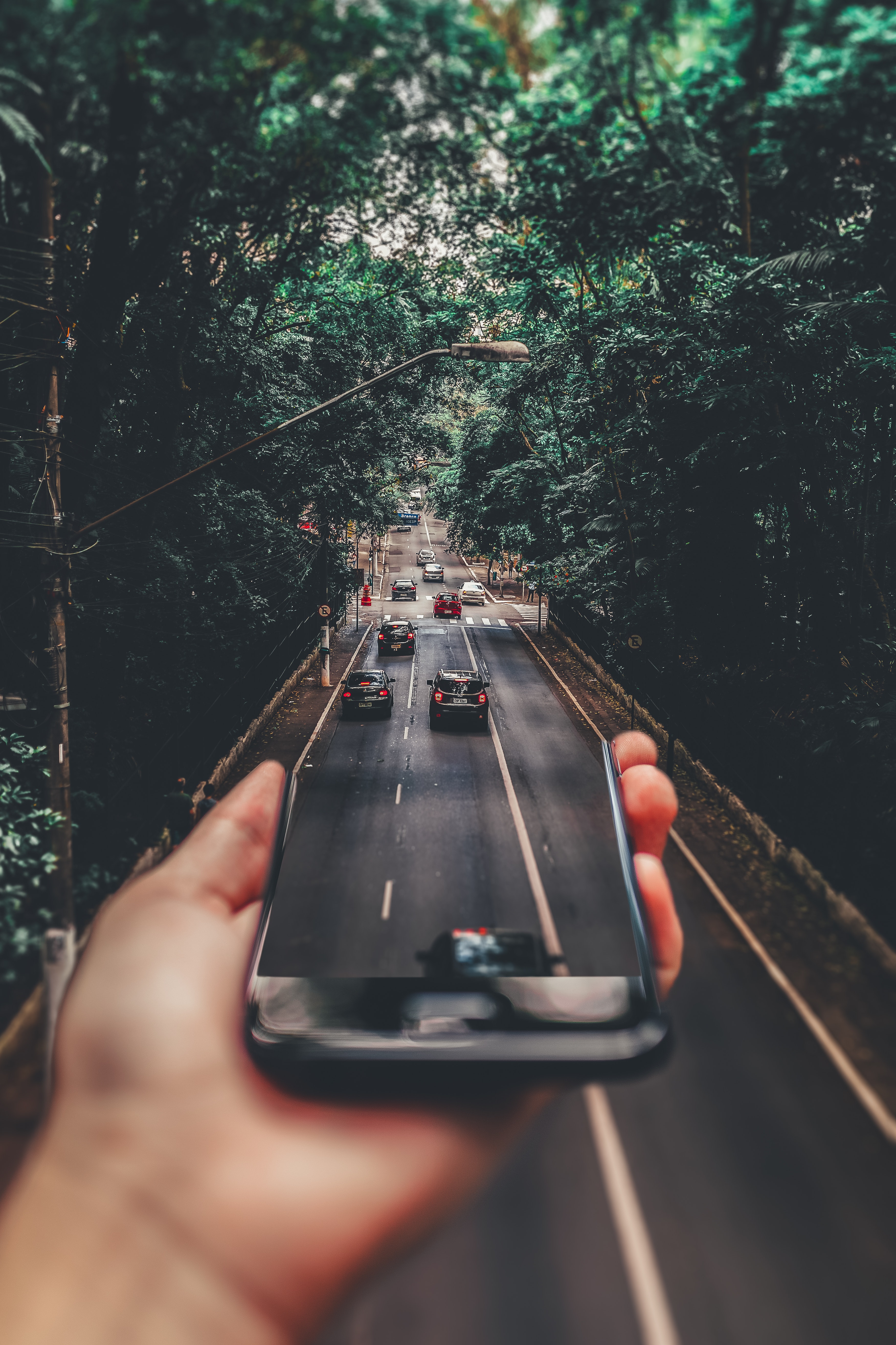 Forced perspective photography of cars running on road below smartphone
