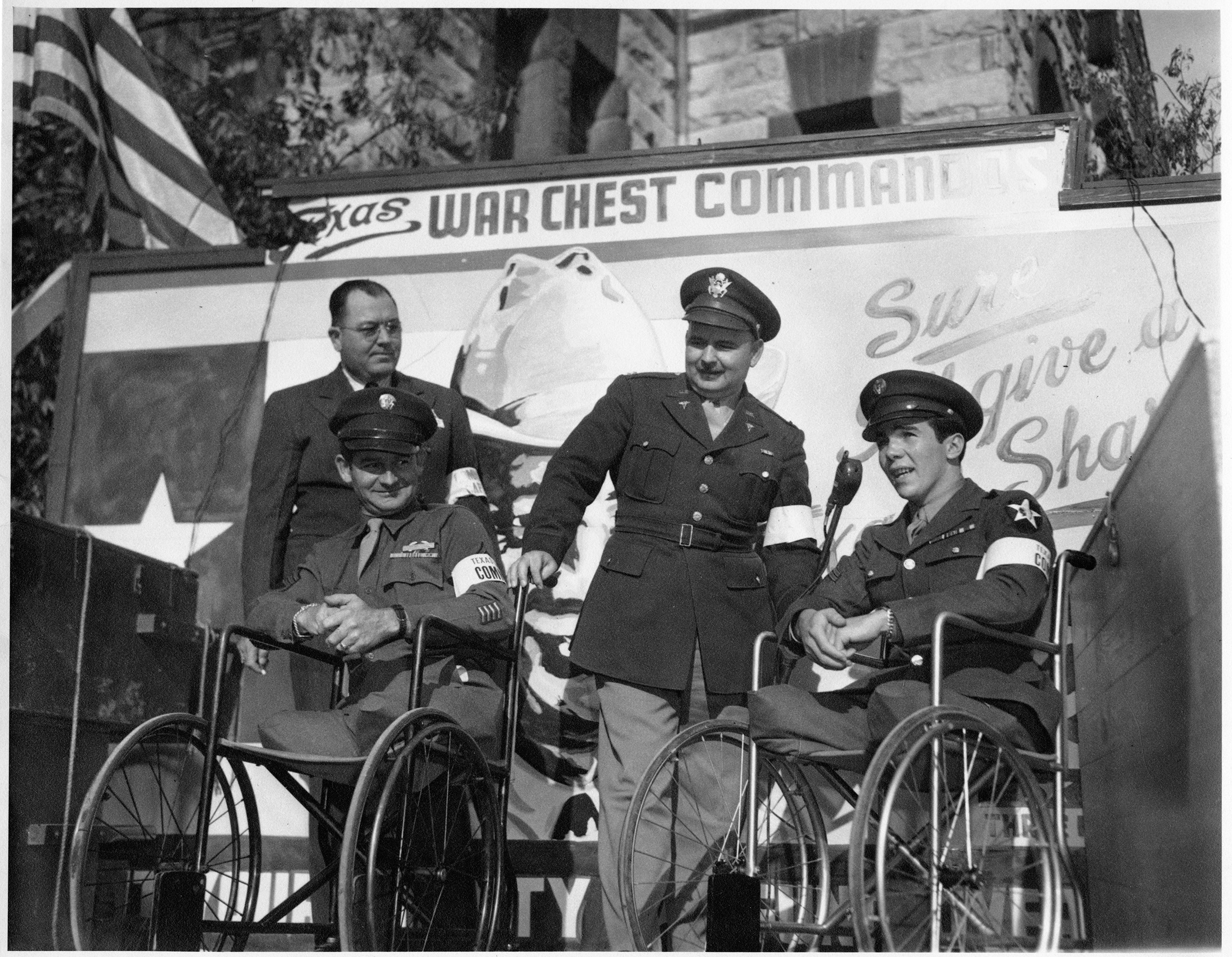 Four men in military uniform pose in front of a poster for the Texas ...