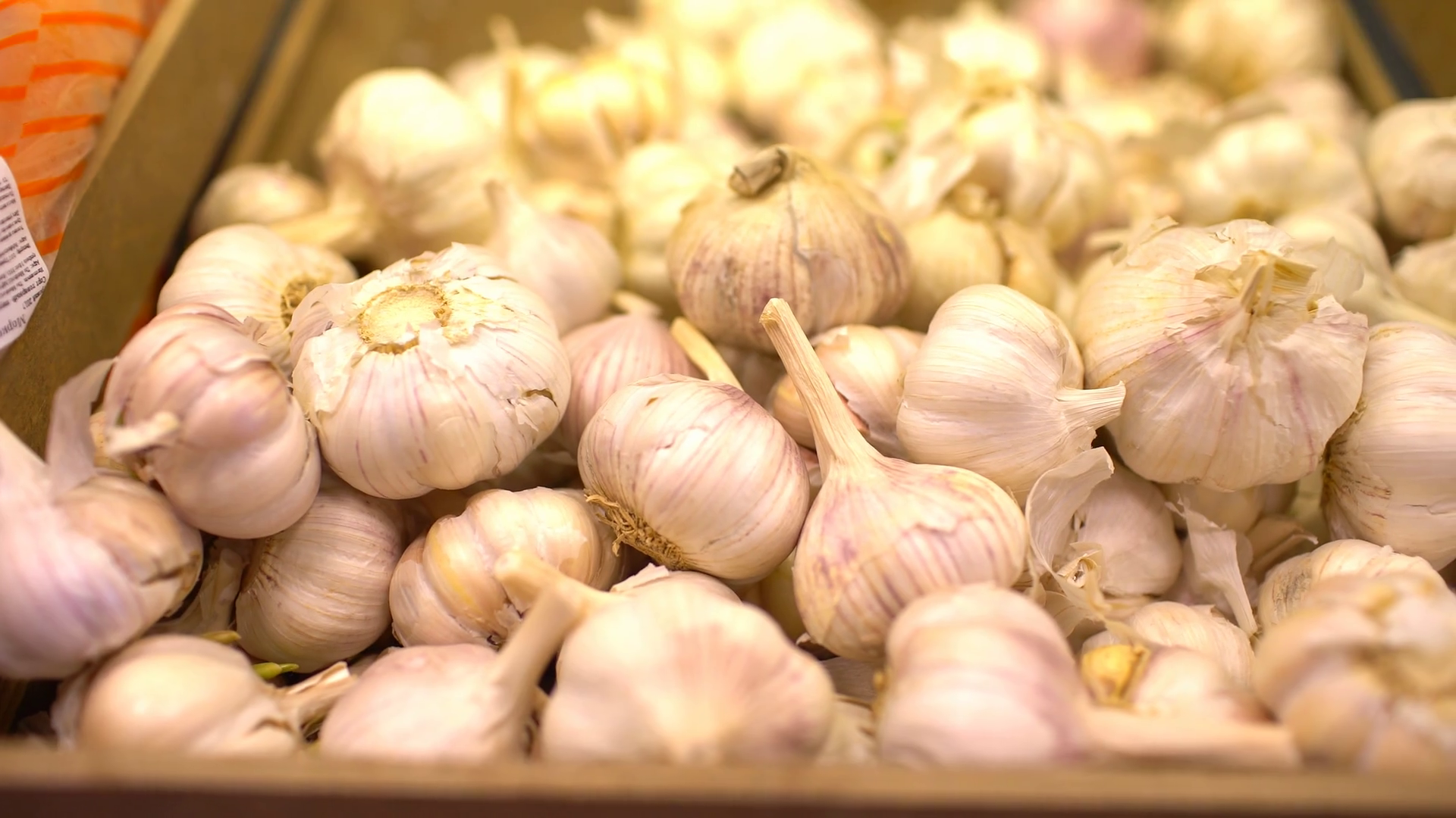Garlic on stand at market place, close up, people passing in the ...