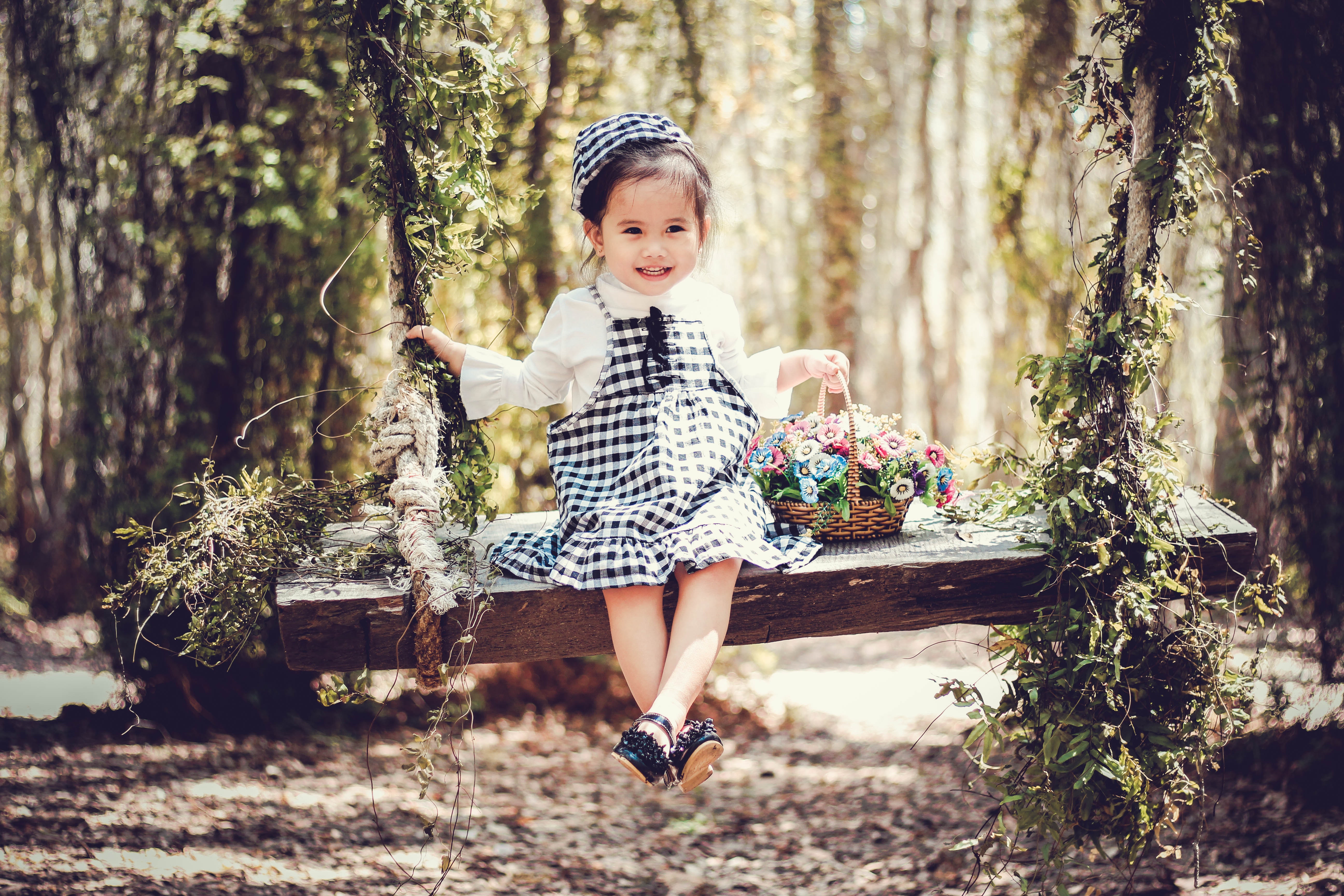 Girl in black and white overall skirt holding basket with petaled flowers photo