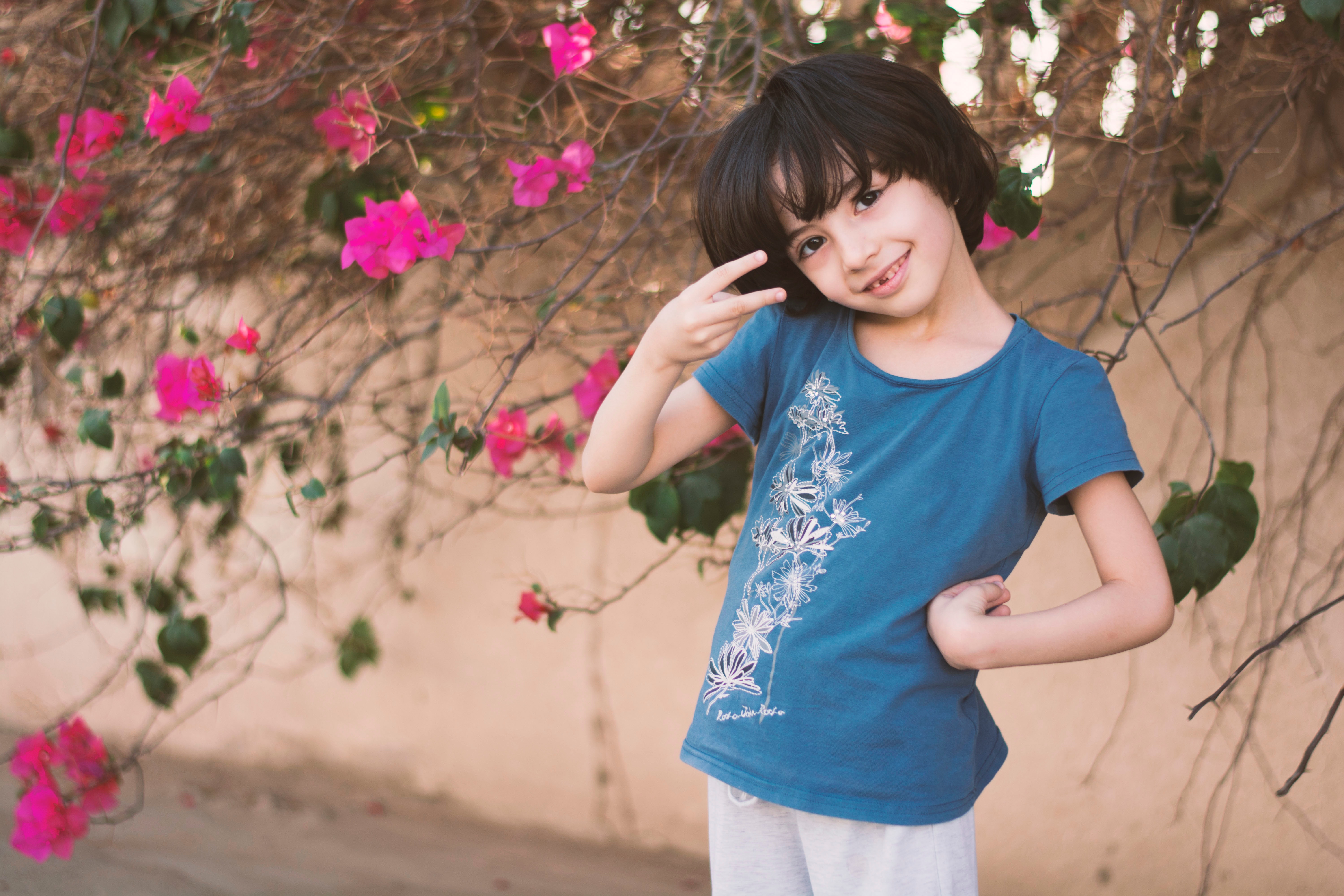 Girl in blue crew-neck t-shirt next to pink petaled flower photo