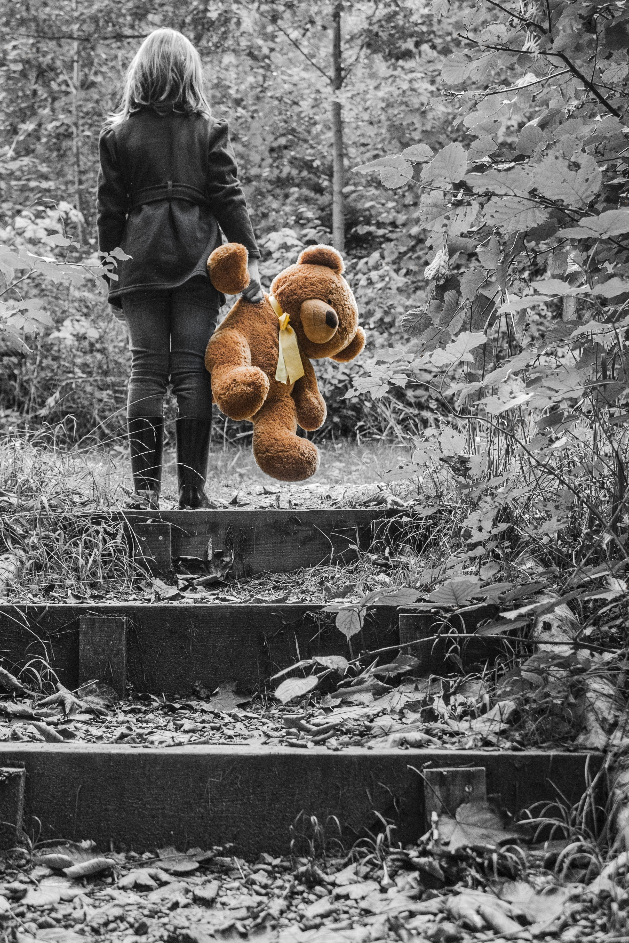 Girl in jacket carrying brown bear plush toy selective color photo