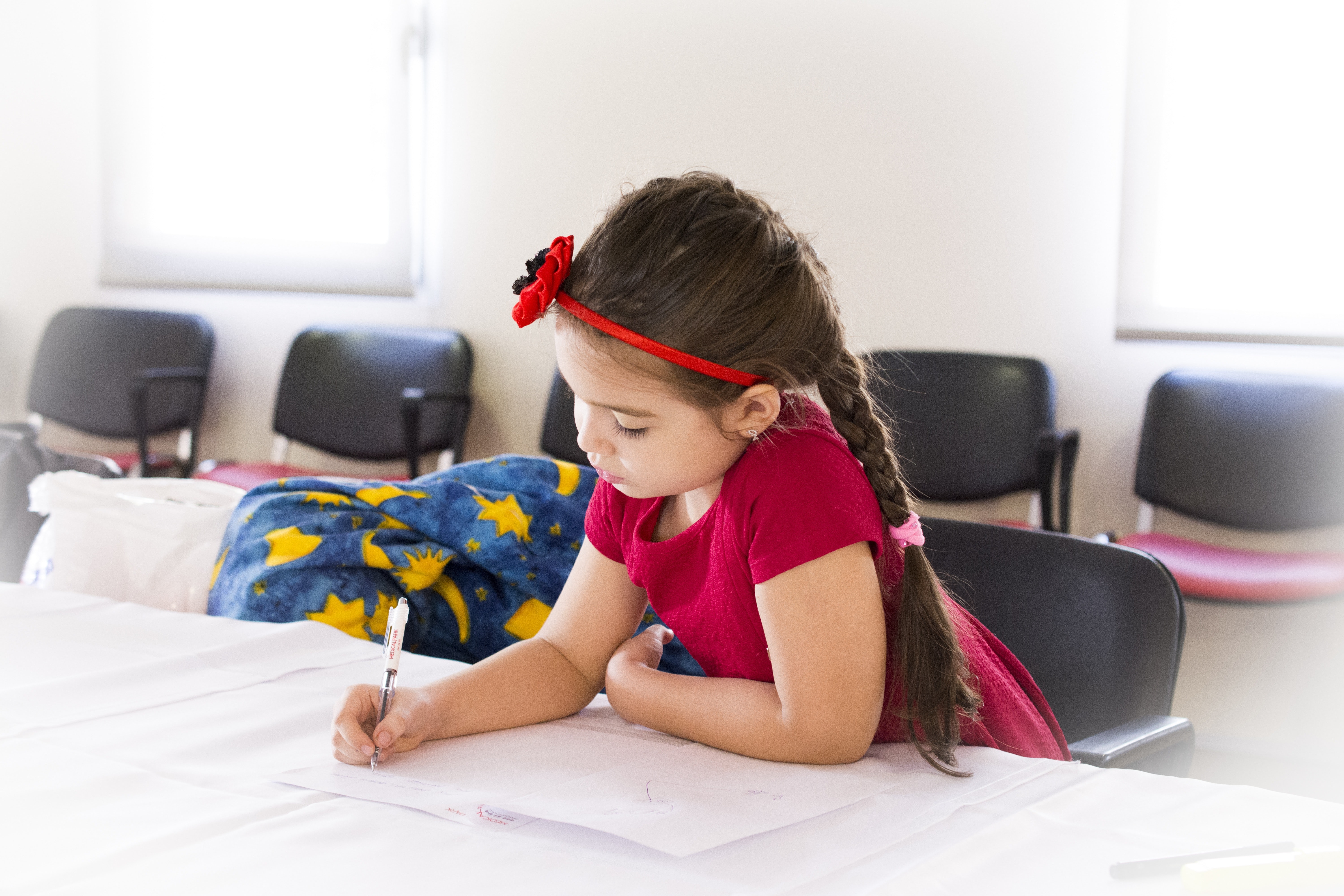 Girl in red short sleeve dress and flower headband holding pen and writing on paper on table photo