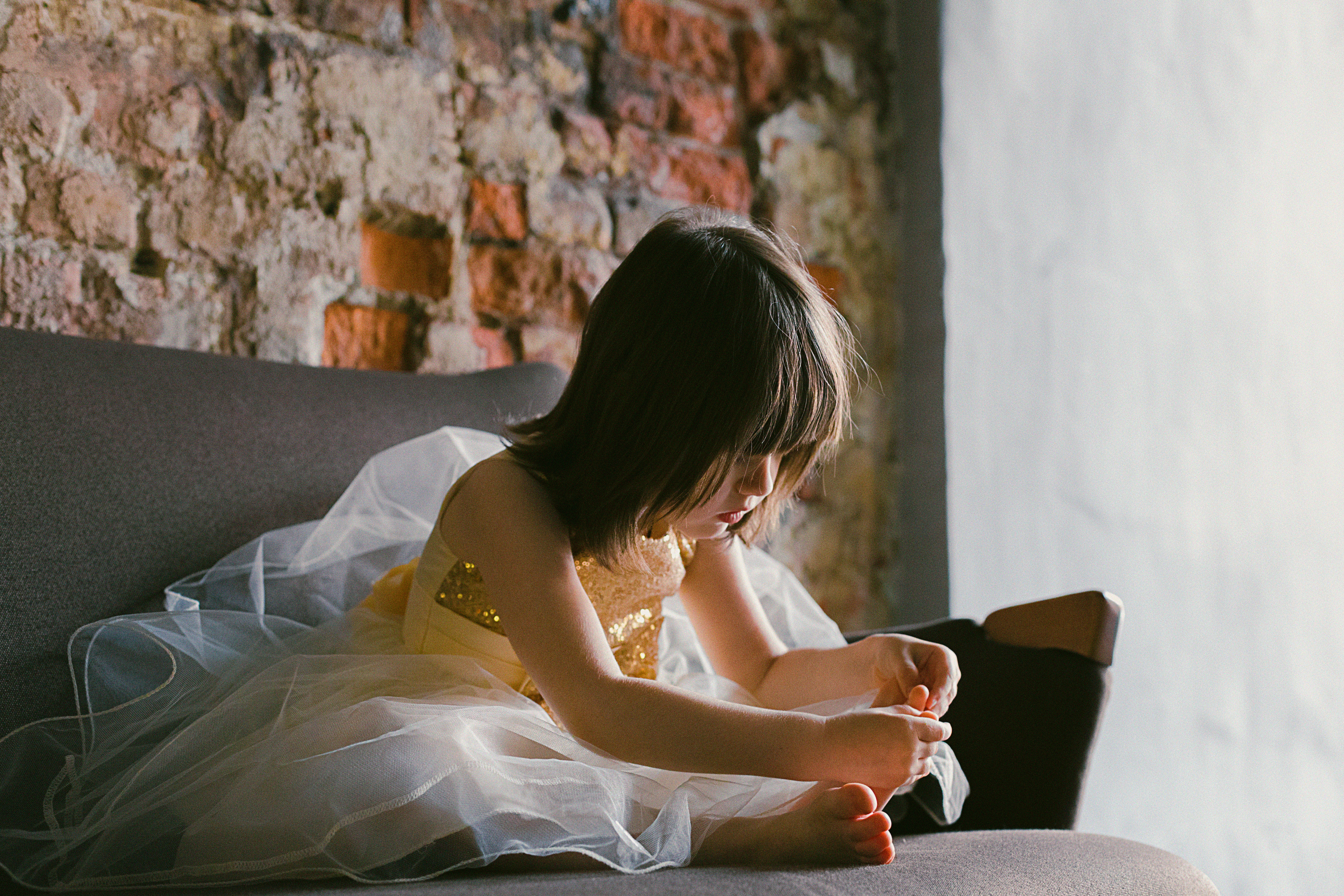 Girl in yellow-and-white dress sitting on couch while holding her foot photo