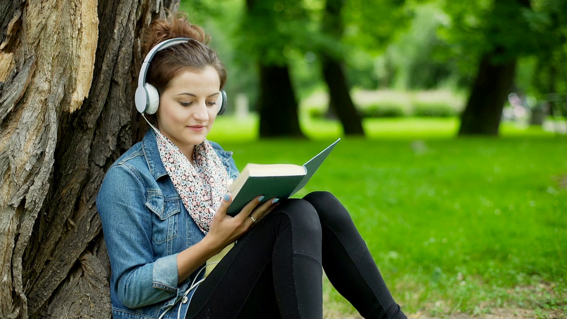 Girl listening music on headphones and reading book in the park ...