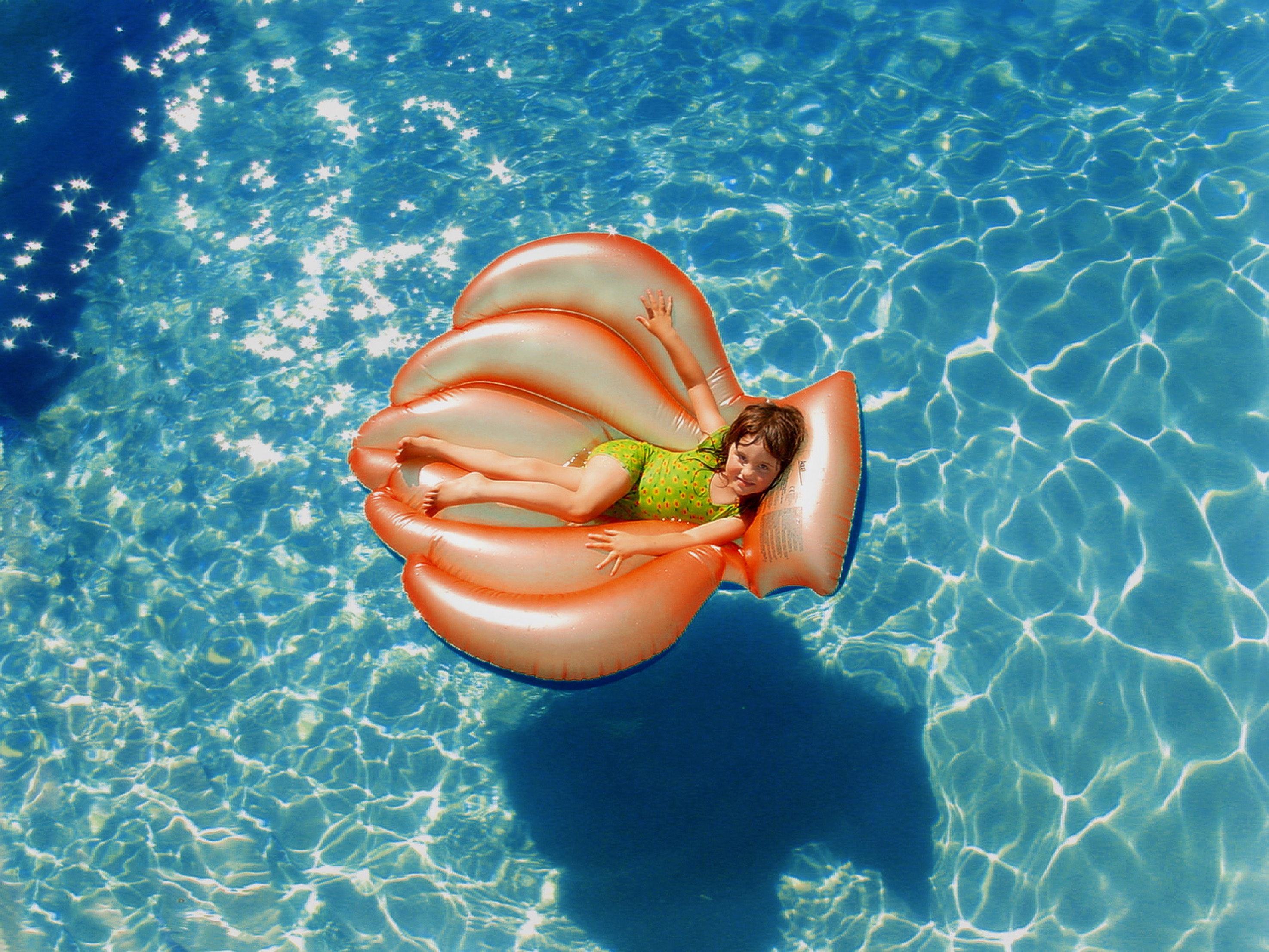 Girl wearing green wet suit riding inflatable orange life buoy on top of body of water photo