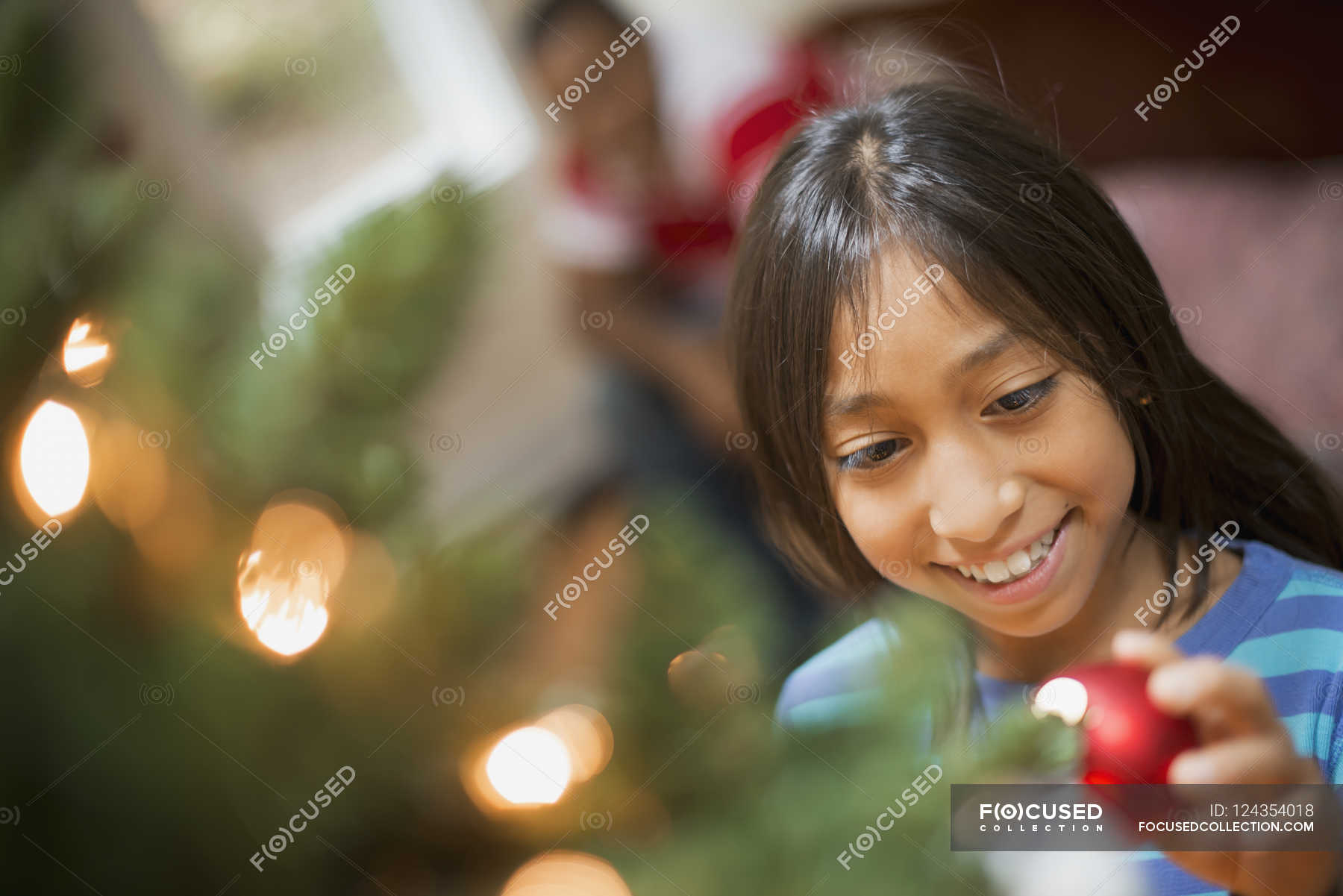 Girl placing bauble on Christmas tree — Stock Photo | #124354018