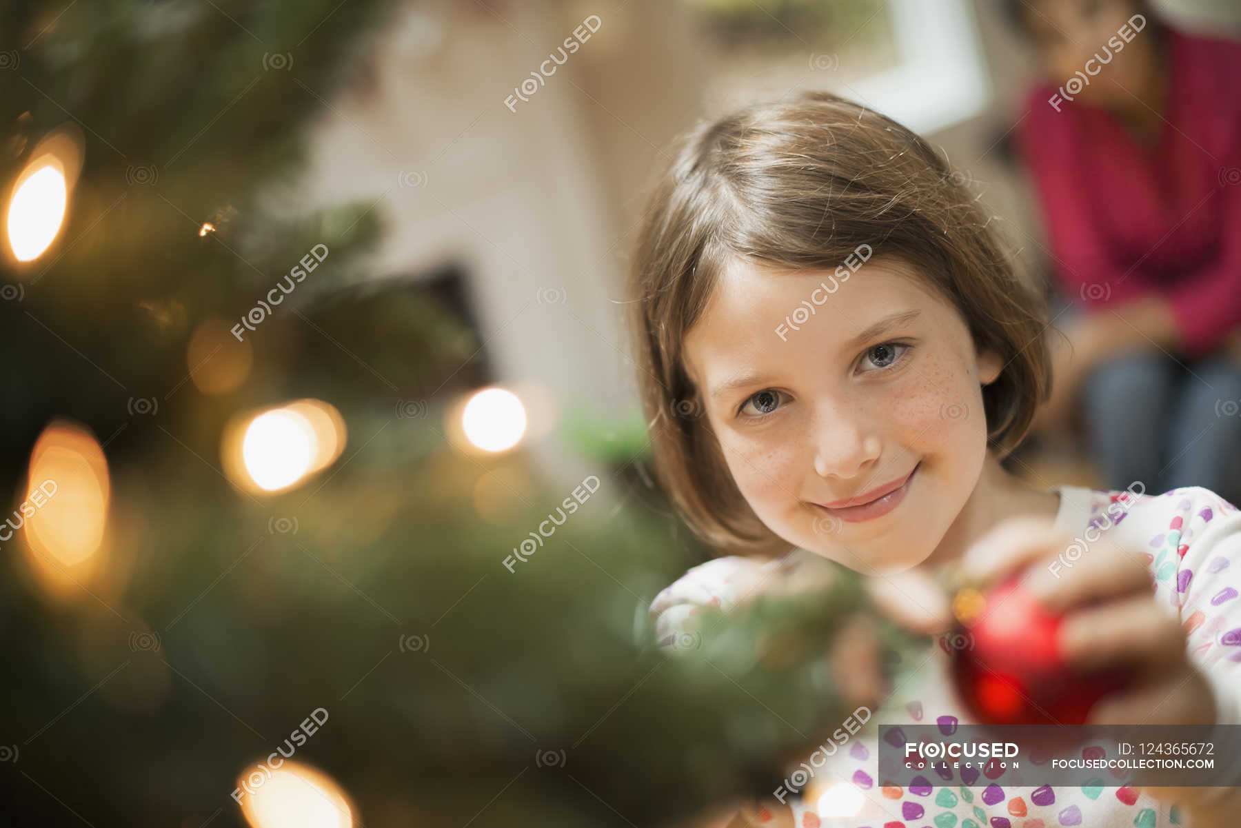 Girl placing bauble on Christmas tree — Stock Photo | #124365672