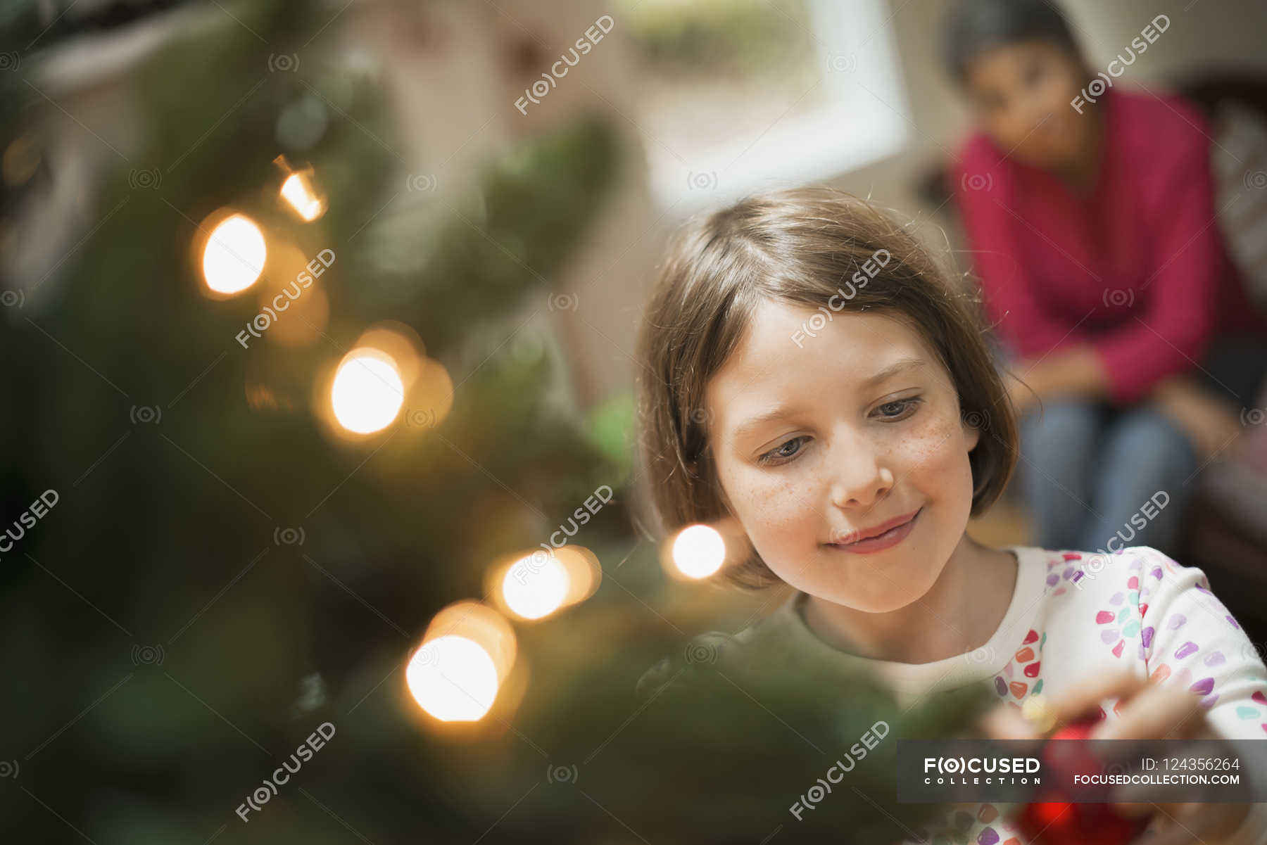 Girl placing bauble on Christmas tree — Stock Photo | #124356264